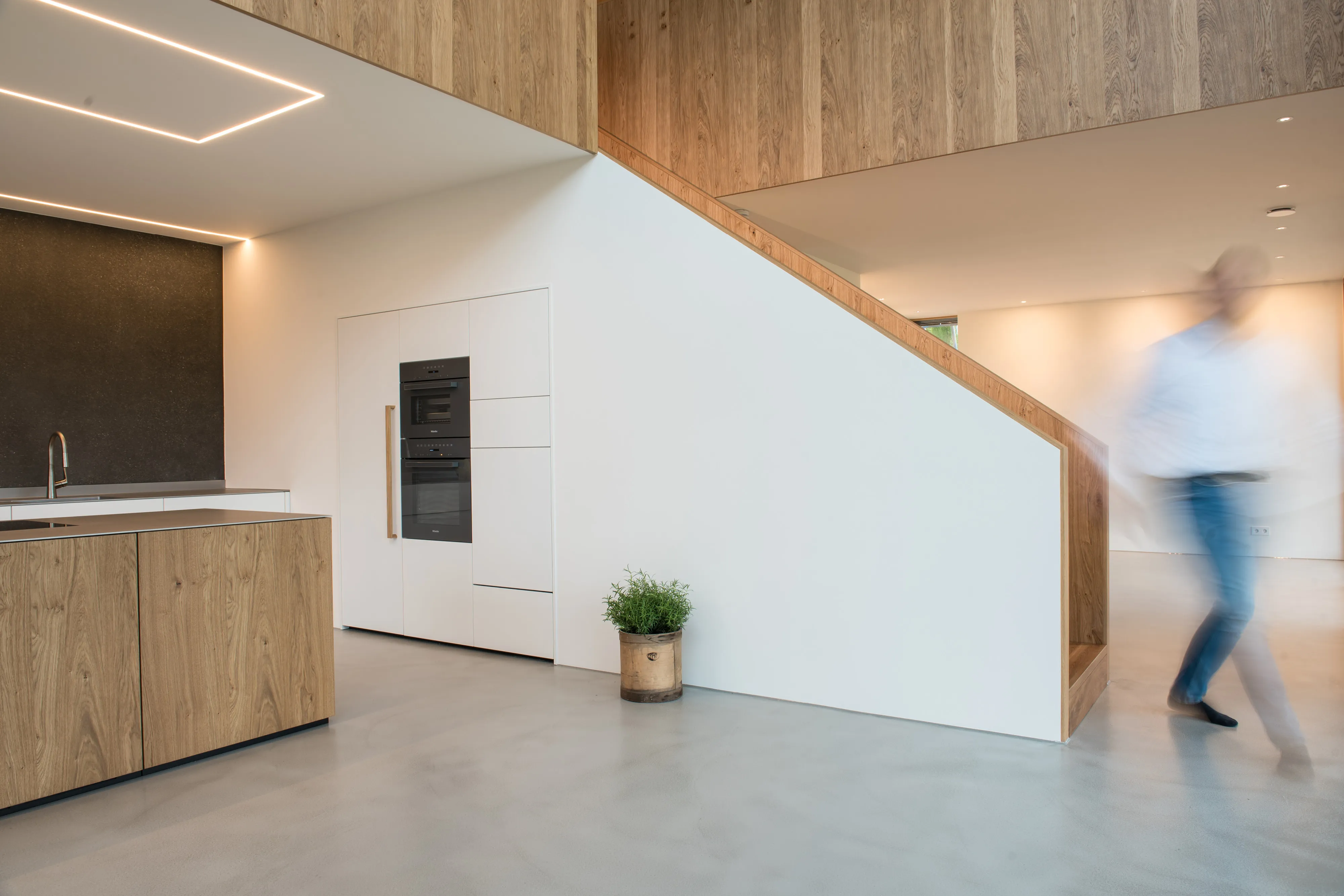 Modernes Küchendesign mit weißem Hochschrank, integrierten Miele-Einbaugeräten und angrenzender Eichenholztreppe