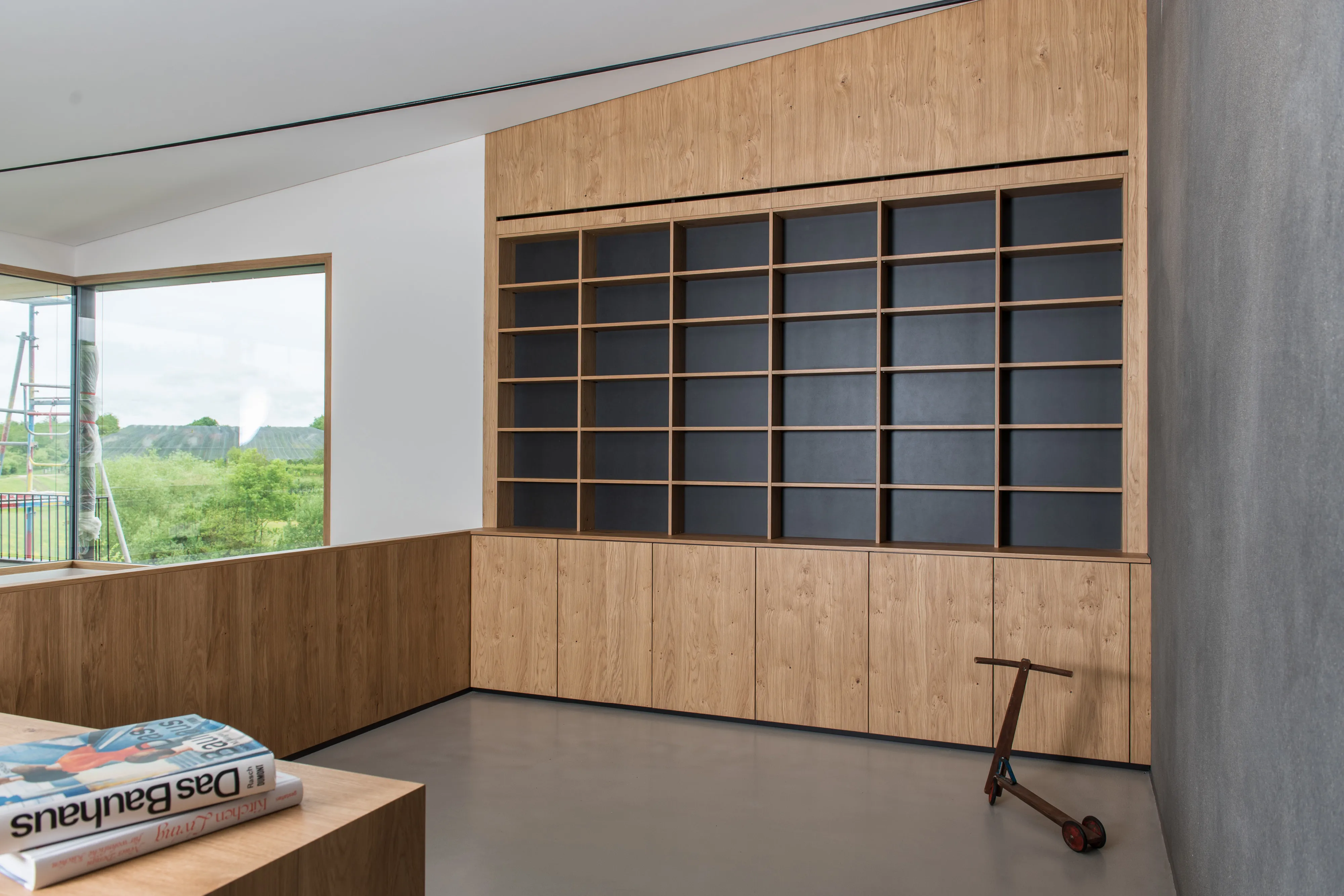 Lichtdurchflutete Galerie mit großem maßgefertigten Wandregal aus Eichenholz, dunklen Regalfächern und Sitzbank