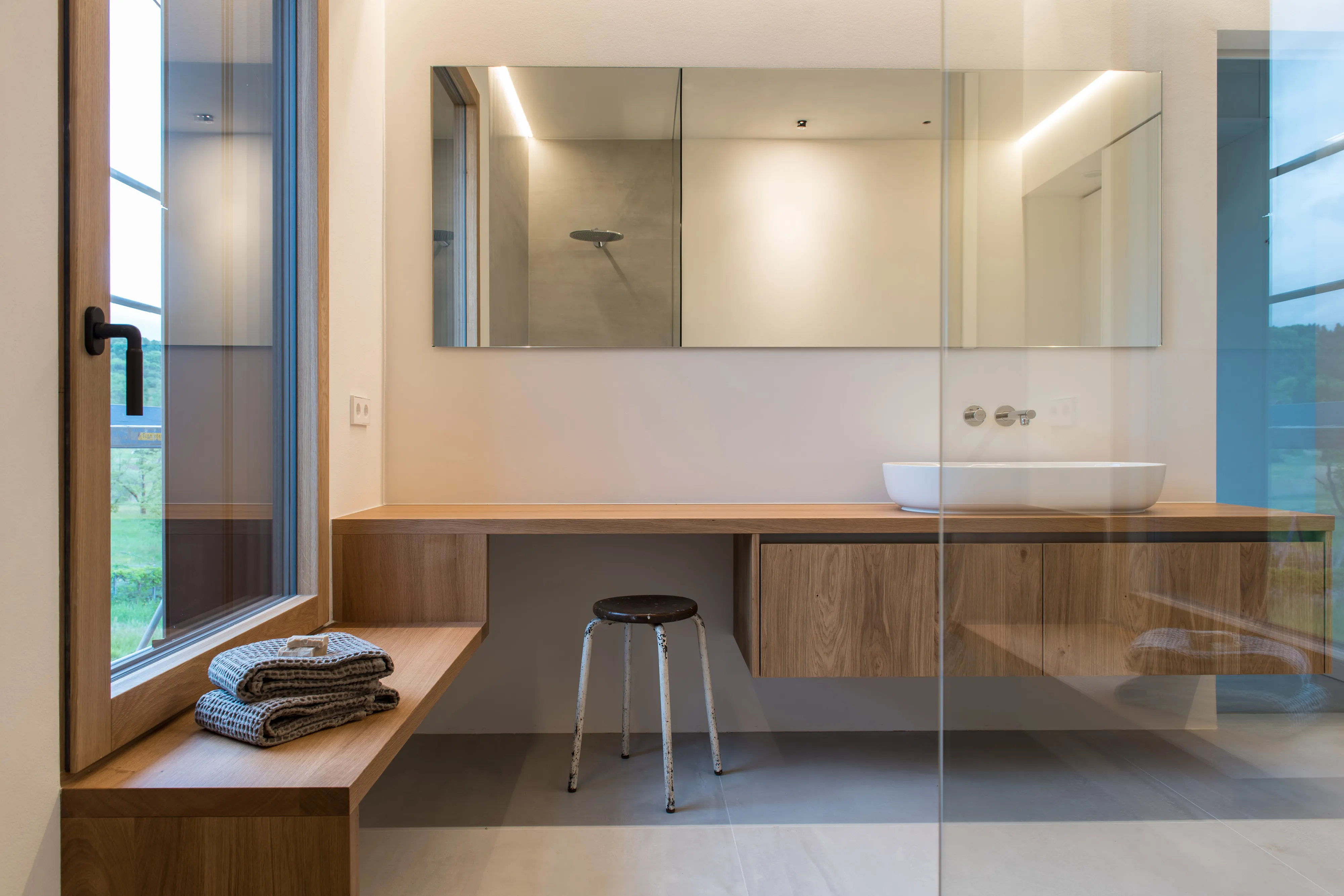 Elegant gestaltetes Badezimmer mit langem Holzwaschtisch, Aufsatzwaschbecken, großem Spiegel und bodentiefer Glasdusche