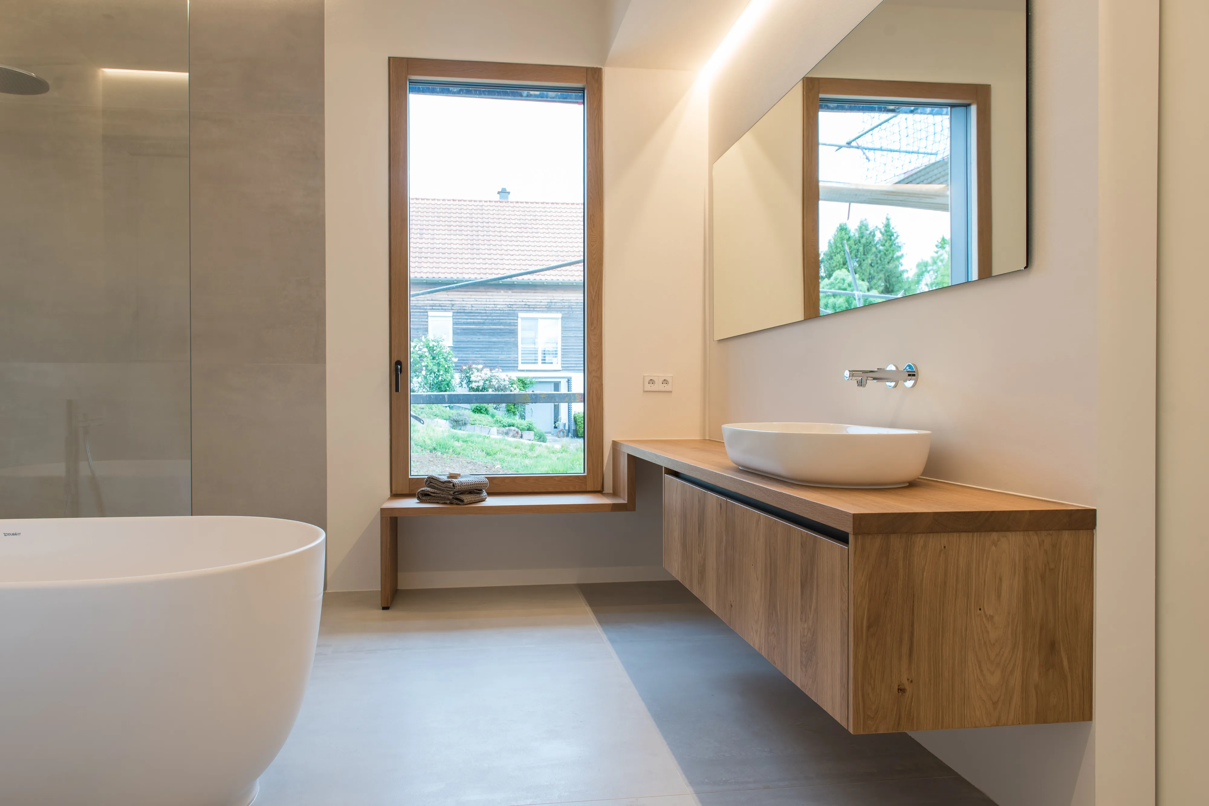 Weiträumiges Badezimmer mit schwebendem Eichen-Waschtisch, großer freistehender Badewanne und bodentiefem Fenster