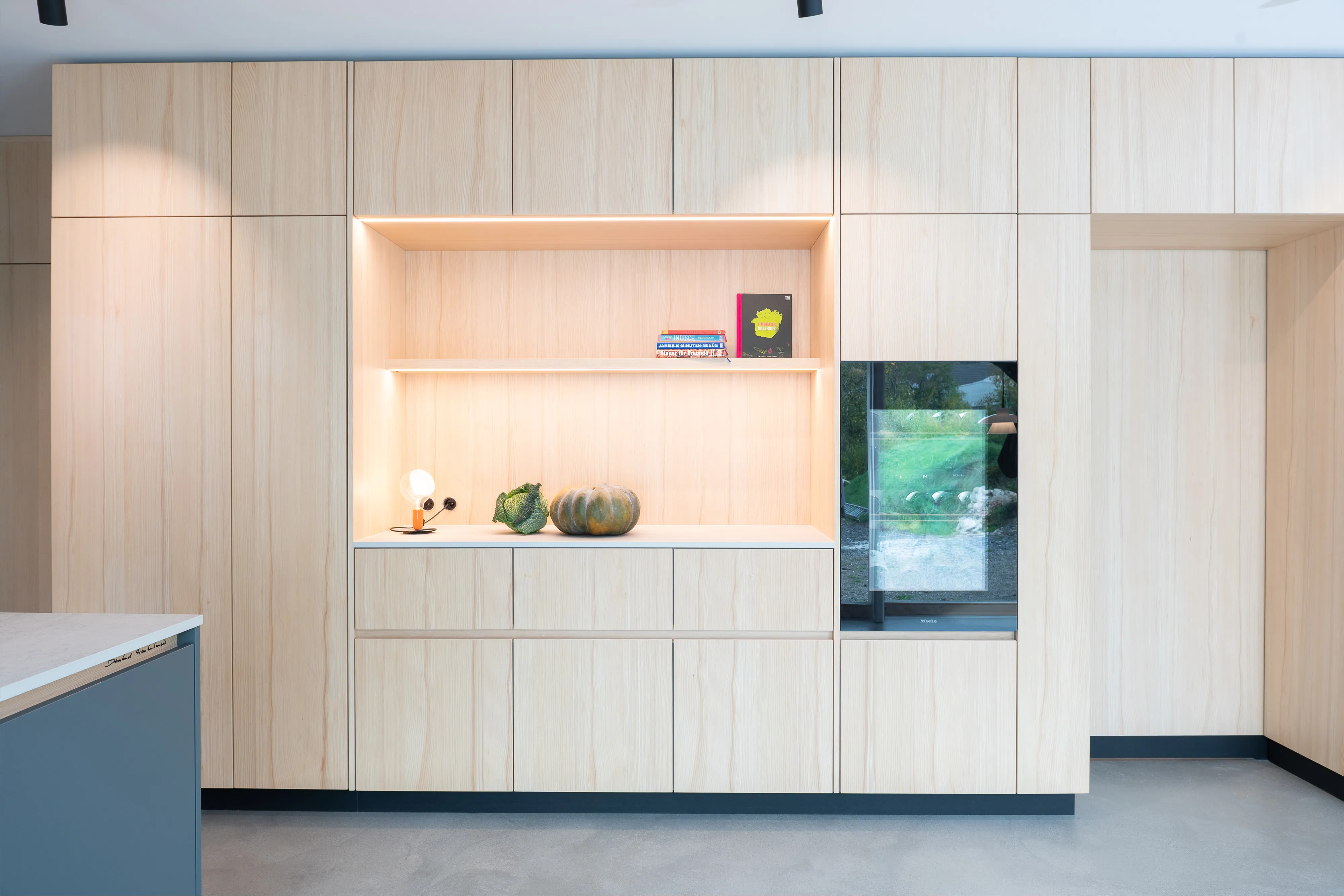 Große helle Holzwand mit beleuchteter Nische, Küchenschränken und integriertem Weinkühlschrank