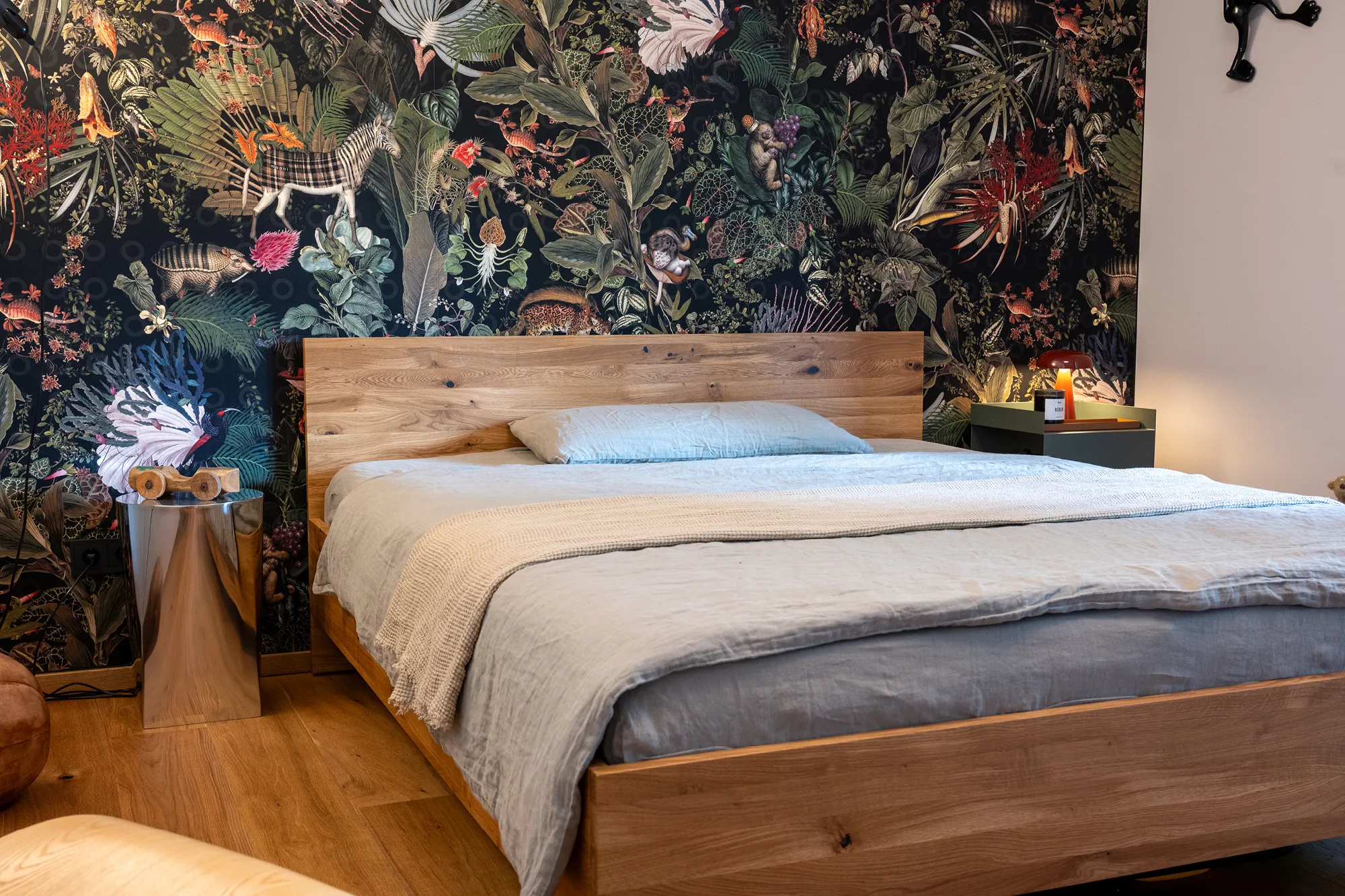 Massivholz-Doppelbett vor einer ausdrucksstarken Wandverkleidung mit Dschungel-Motiv.