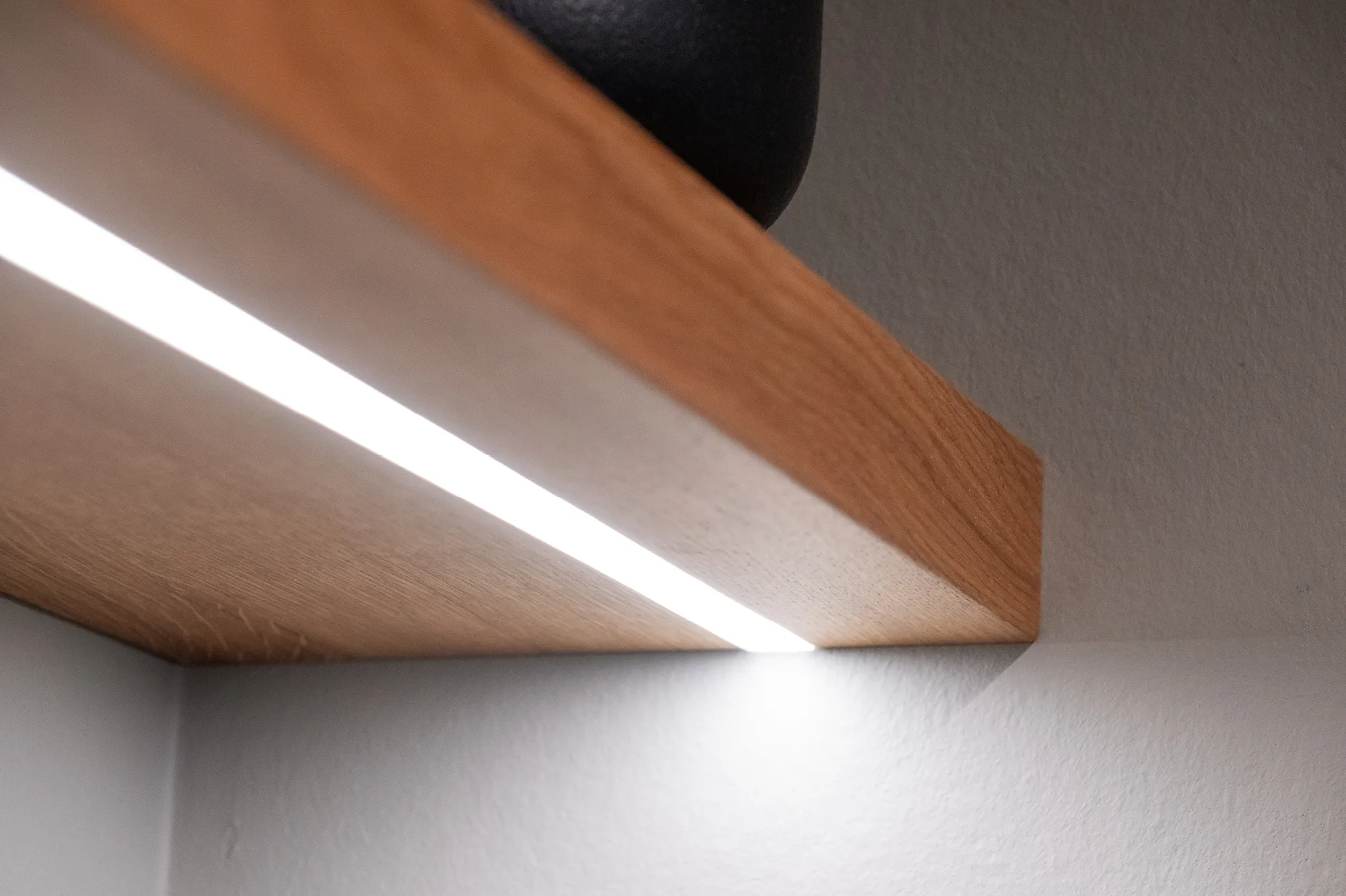Eichenholz-Wandregal mit bündig eingelassenem LED-Lichtstreifen an der Unterseite.