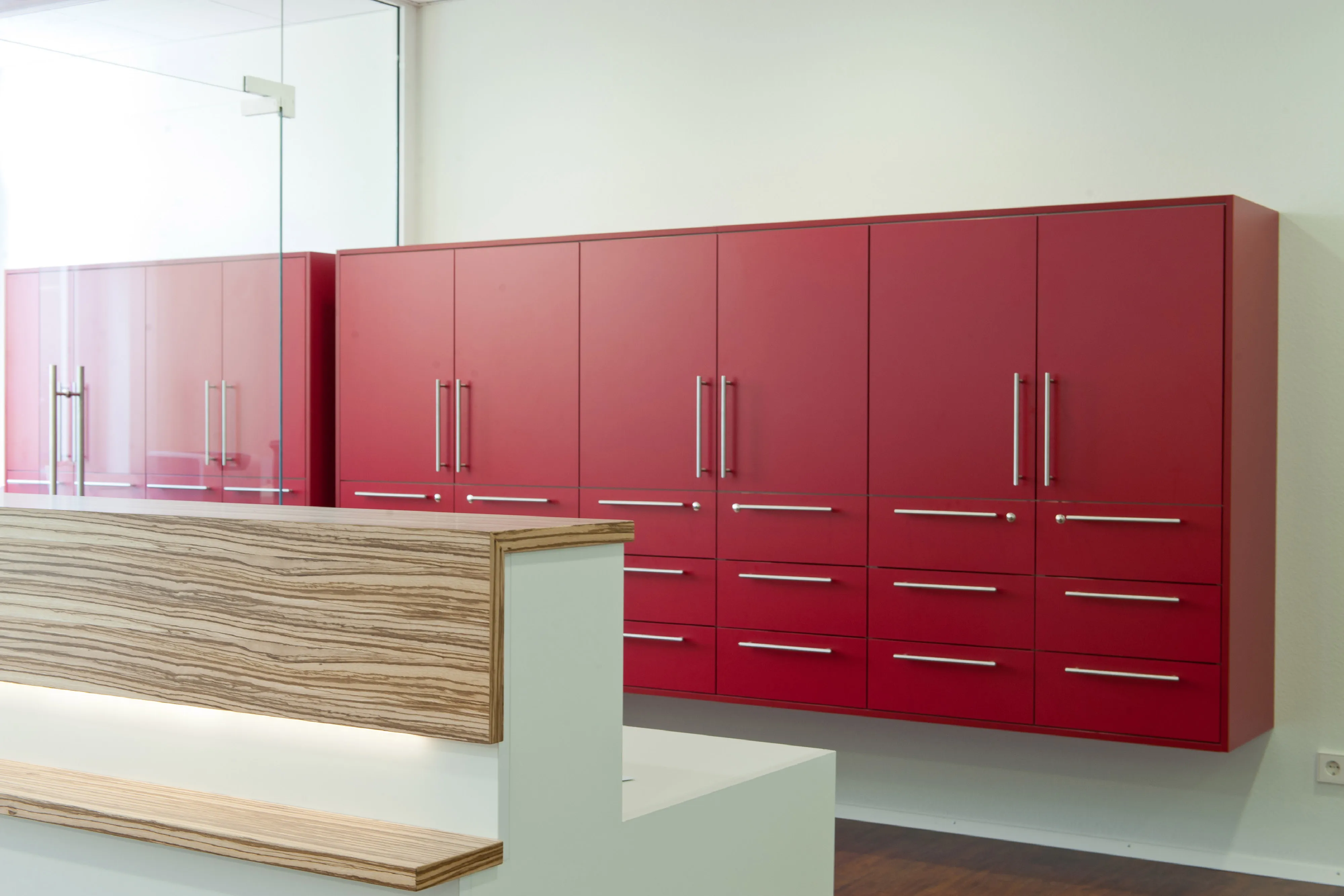 Rezeption mit Blick auf eine große, wandhängende Einbauschrank-Wand in kräftigem Rot mit silbernen Metallgriffen.