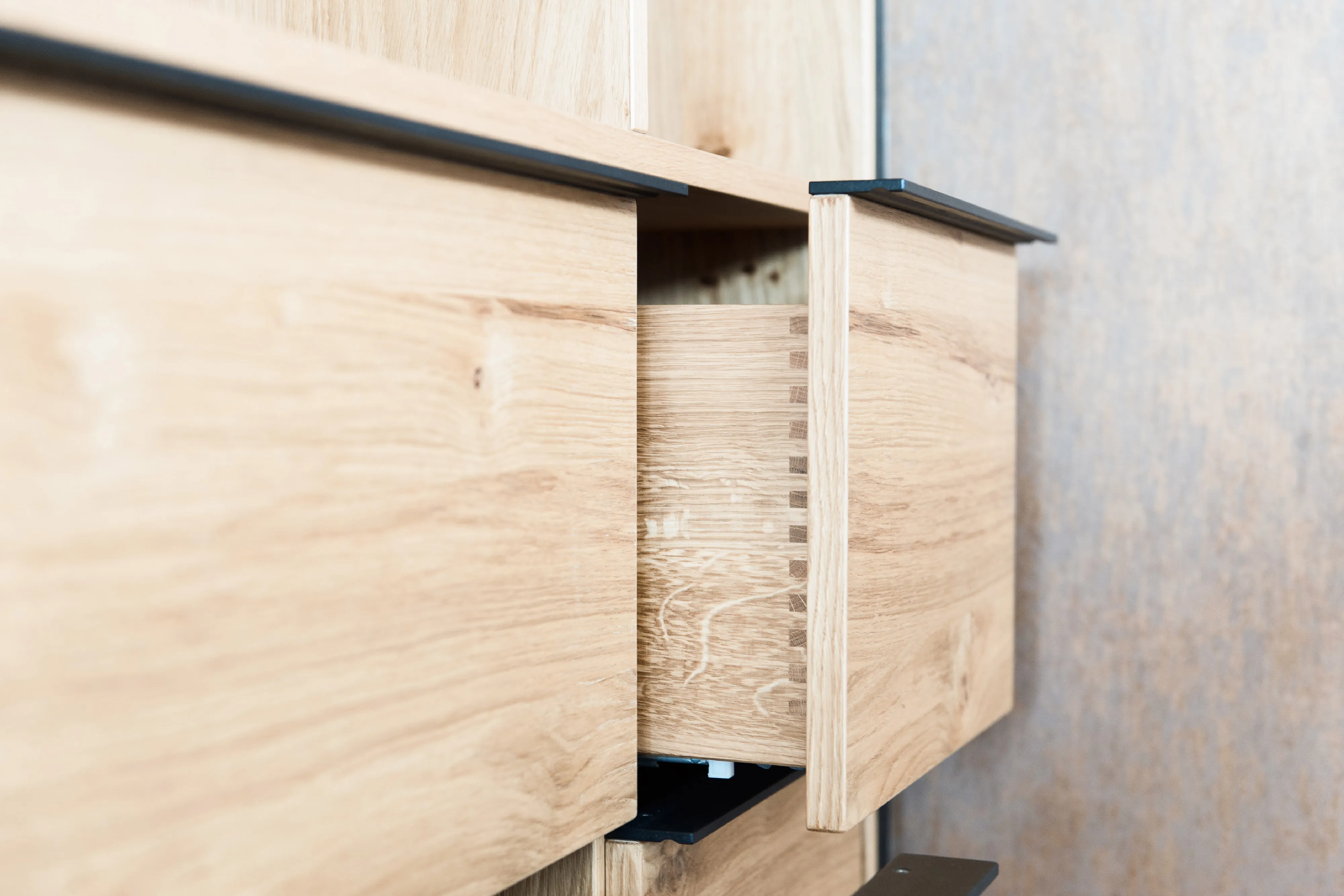 Nahaufnahme einer leicht geöffneten Holzschublade aus Eiche mit präziser Zinkenverbindung und schwarzer Griffleiste.