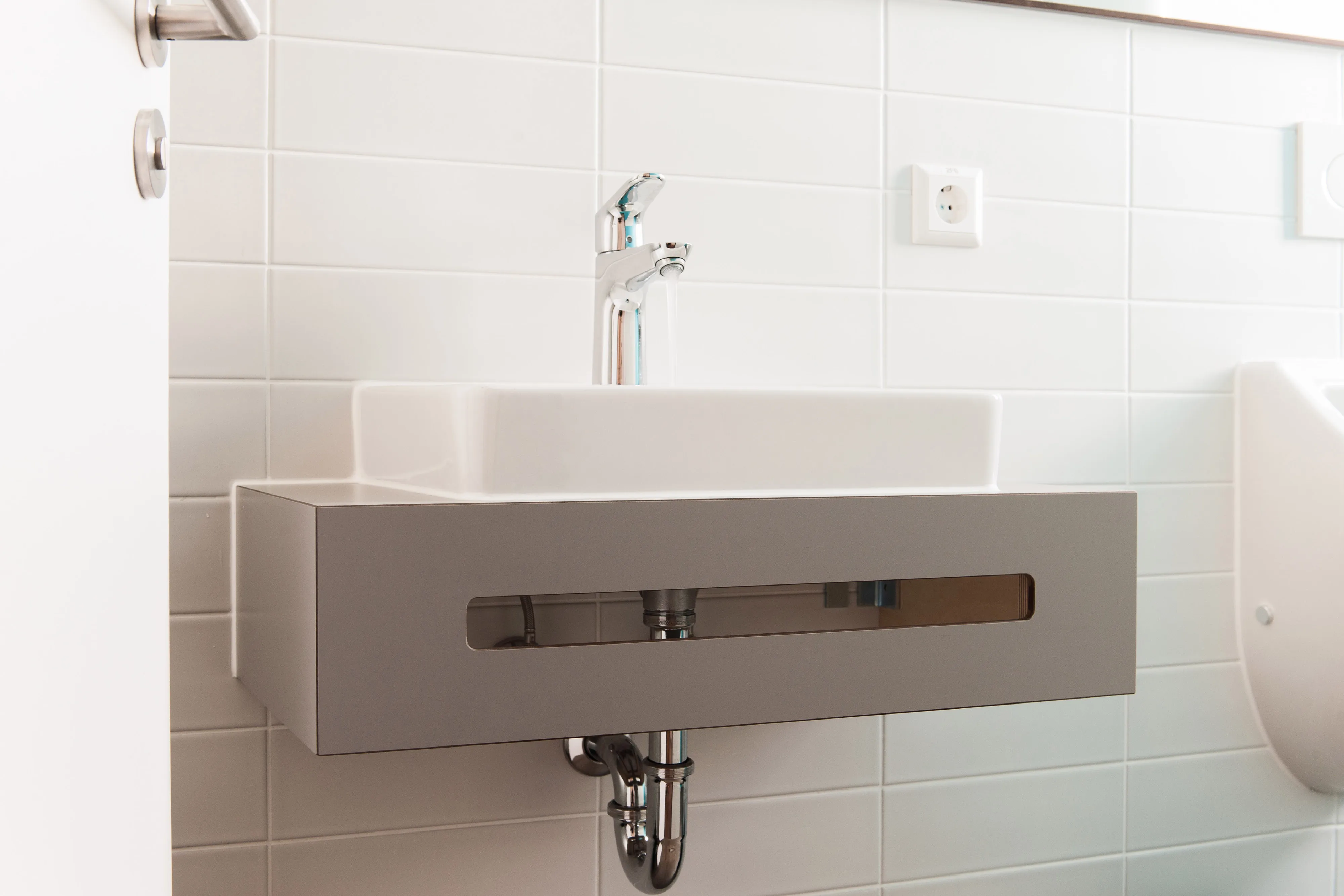 Nahaufnahme des Waschtischs mit grauem Unterbau, Handtuchöffnung und verchromter Armatur im Sanitärbereich.