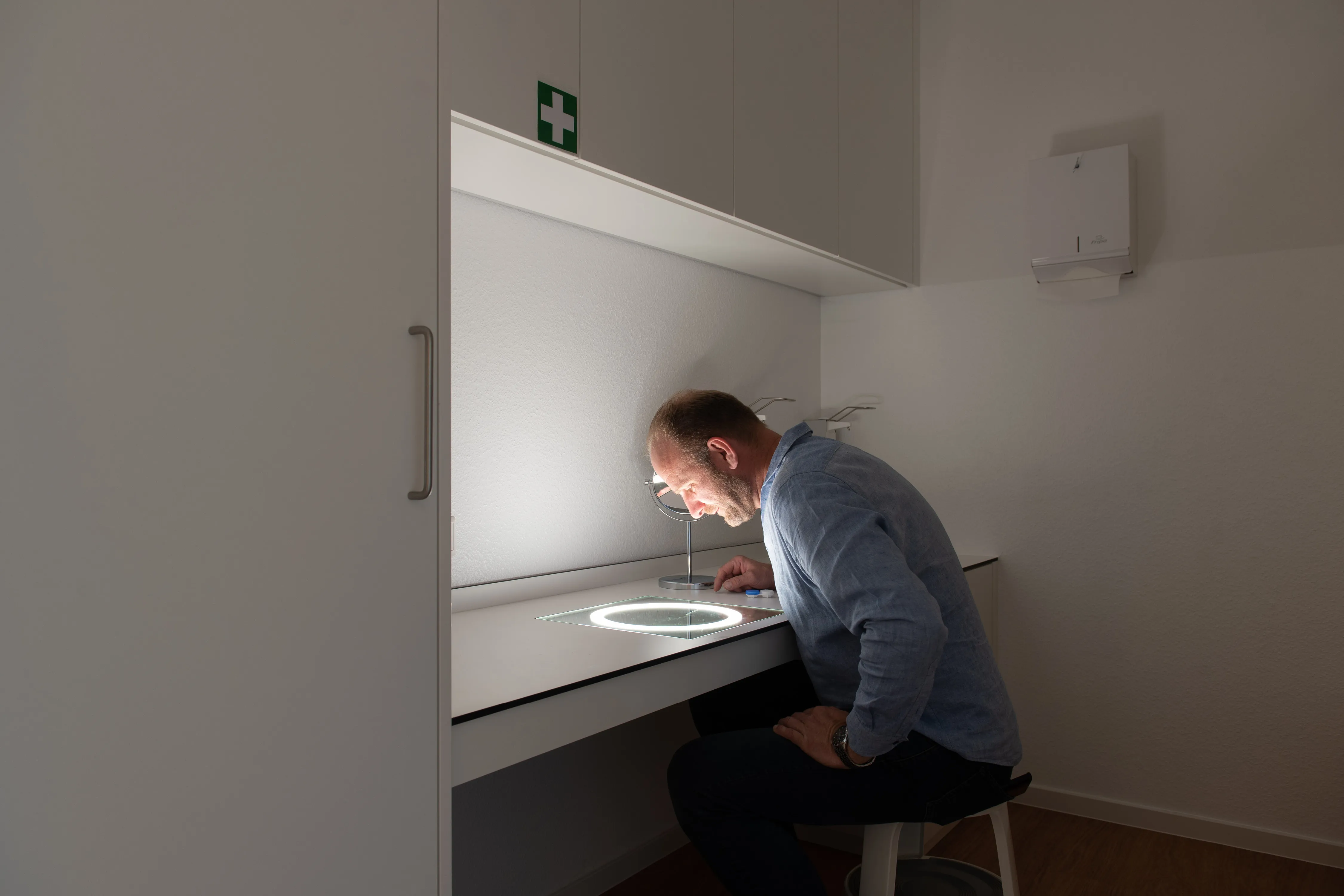 Mann sitzt am maßgefertigten Kontaktlinsen-Arbeitsplatz mit integrierter Leuchtplatte in der Tischfläche.