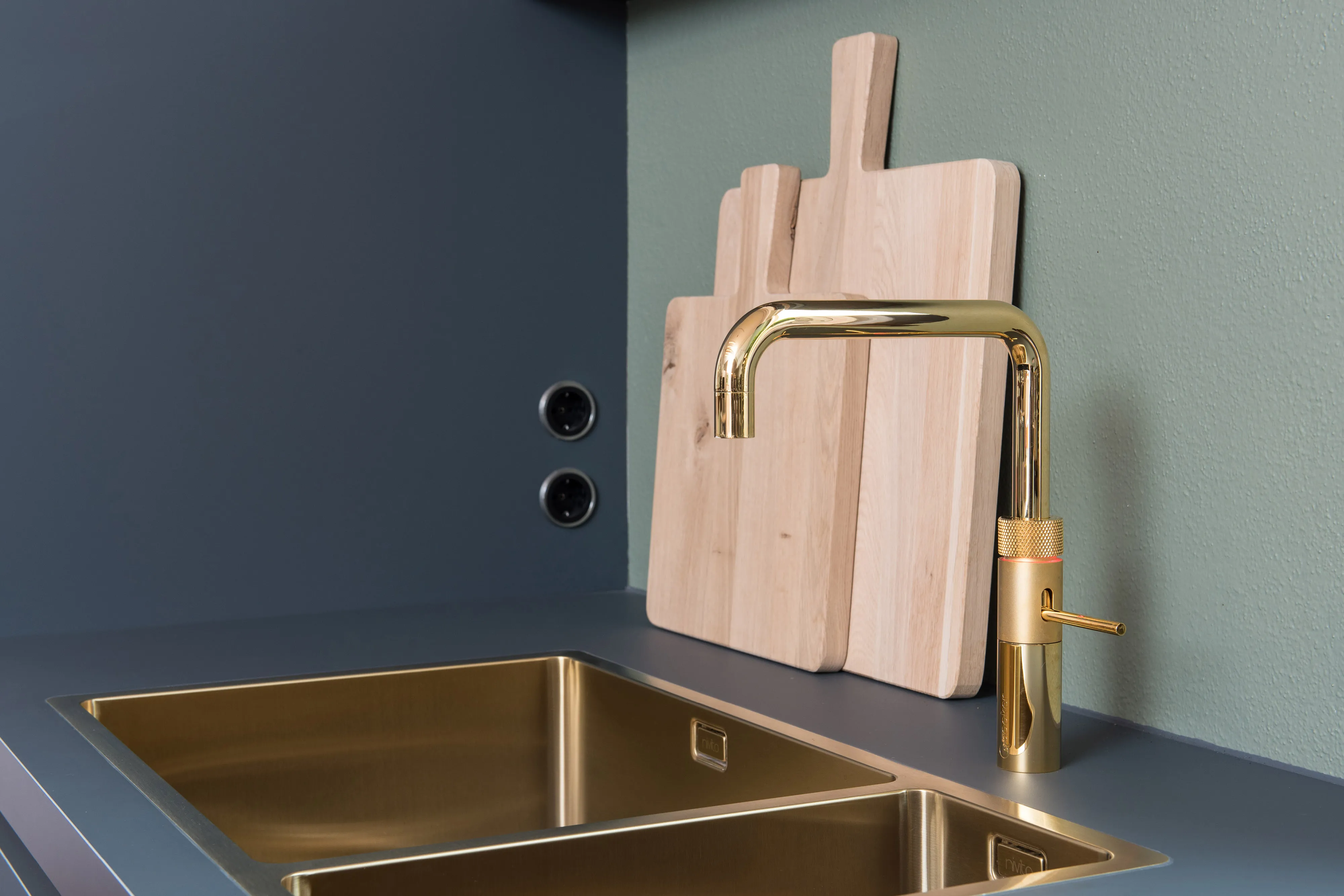 Messing-Wasserhahn und Doppelspülbecken in goldener Optik auf dunkelgrauer Arbeitsplatte