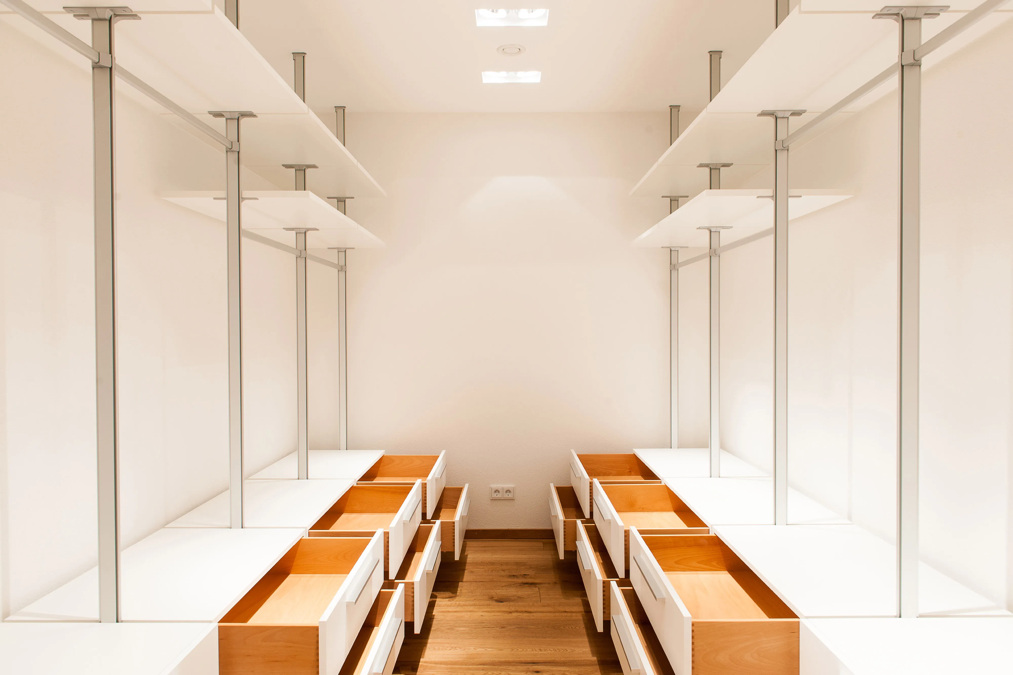 Begehbarer Kleiderschrank mit zwei gegenüberliegenden Regalzeilen, weißen Fronten und geöffneten Holzauszügen.