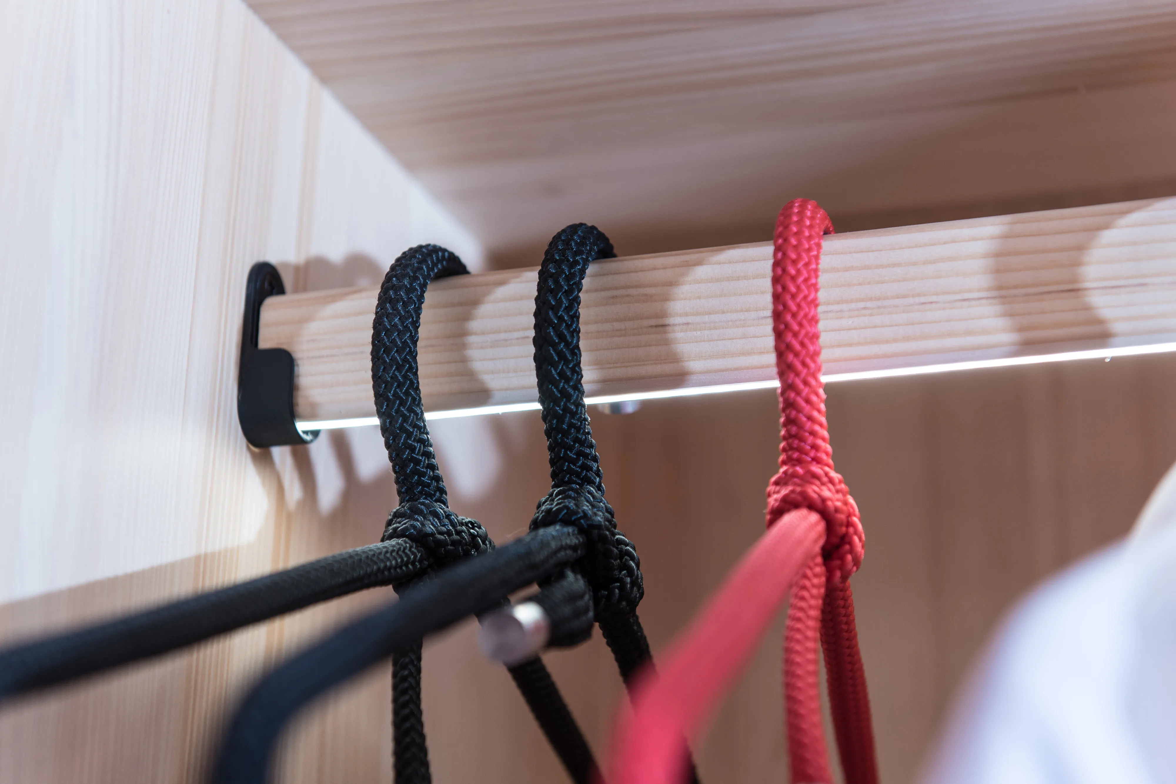 Nahaufnahme einer Garderobenstange aus Holz mit integrierter LED-Leiste und Kordel-Kleiderbügeln.