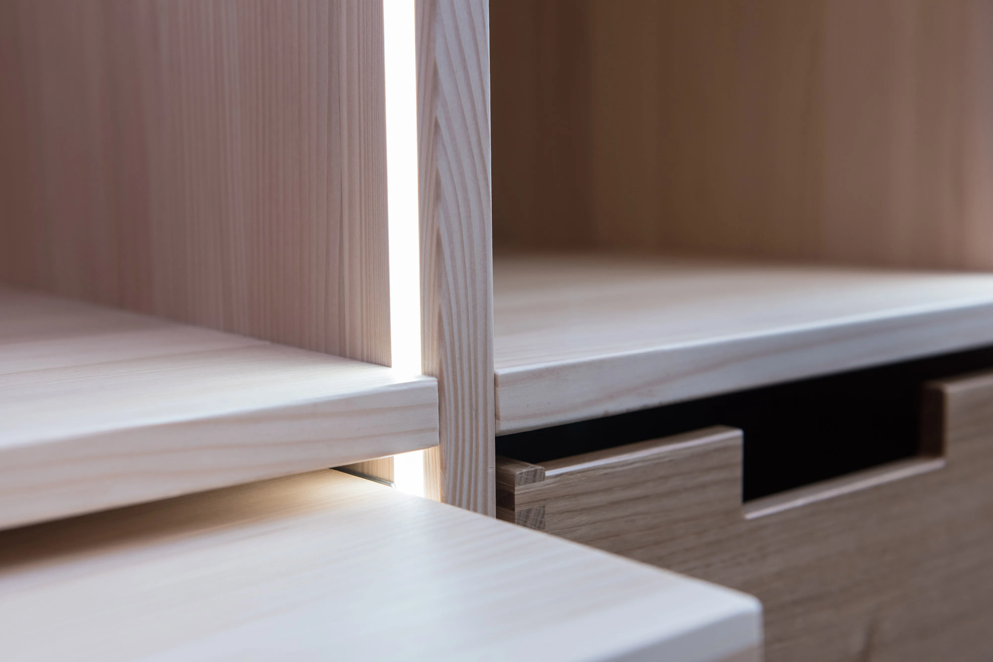 Präzise handwerkliche Detailaufnahme von gezinkten Holzfächern, Auszügen und verdeckten Fugenbeleuchtungen.