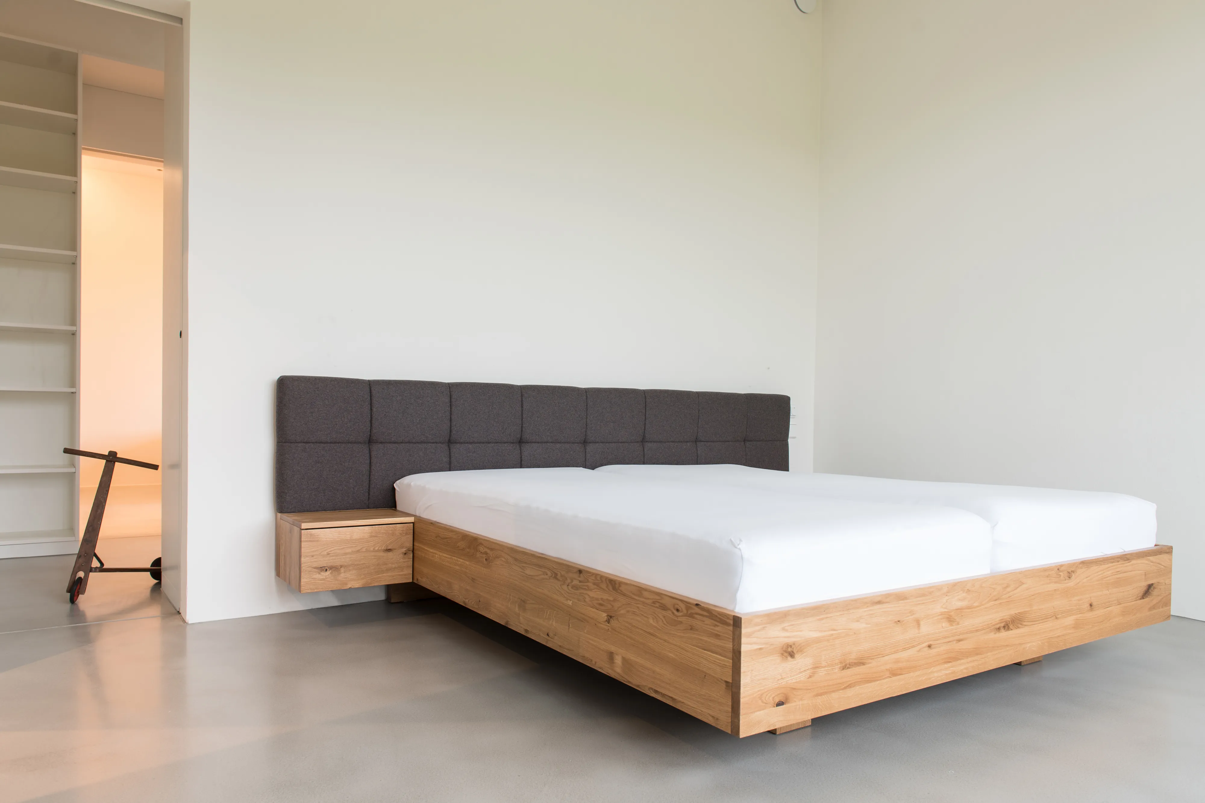 Modernes Eichenholz-Doppelbett mit schwebender Optik, dunklem Polsterkopfteil und integrierter Nachtkonsole.