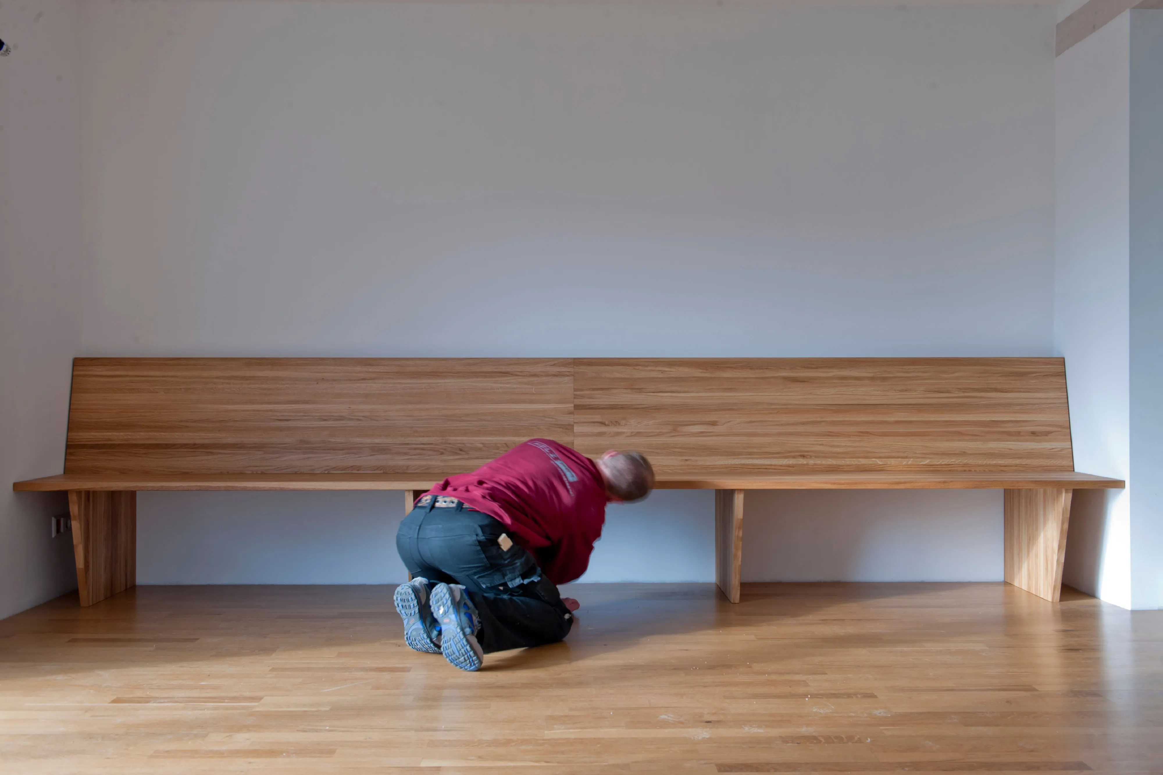 Schreiner kniet vor einer langen Wandbank aus Holz während der Montage im Innenraum.