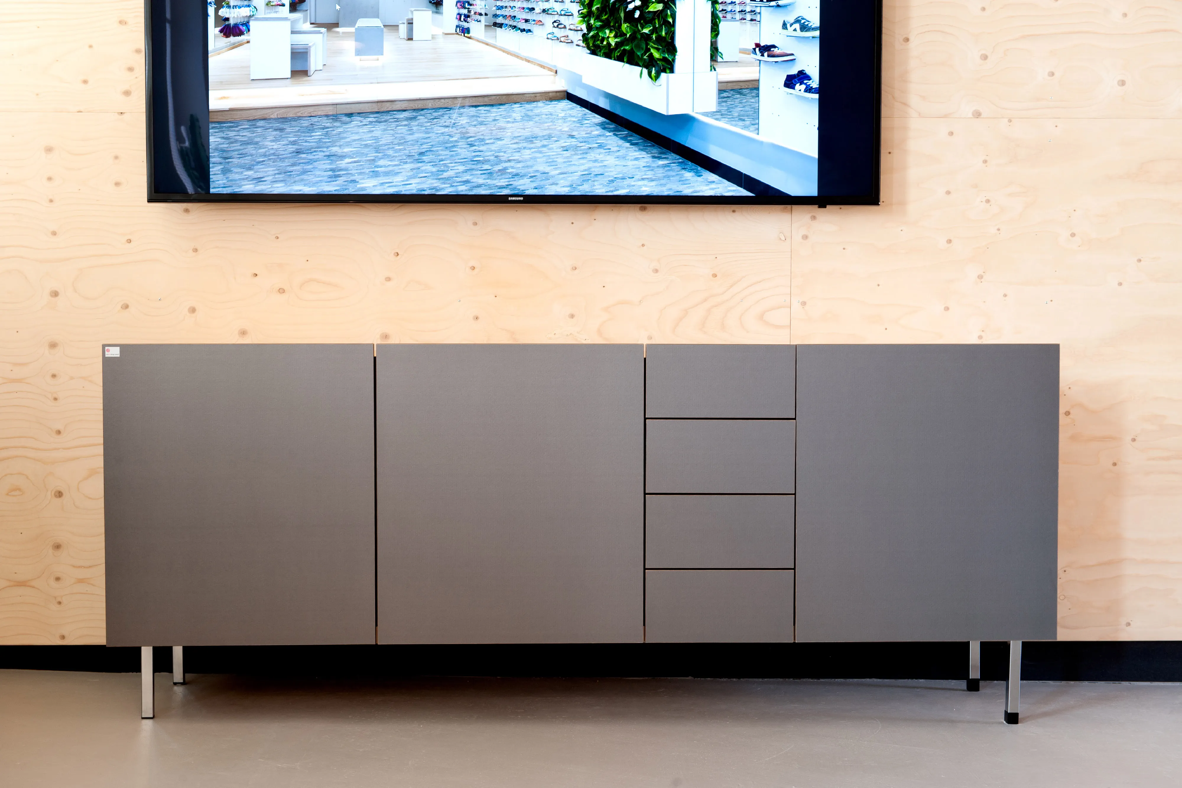 Graues, maßgefertigtes Sideboard mit Schubladen und Türen auf feinen Metallfüßen unter einem TV-Bildschirm.