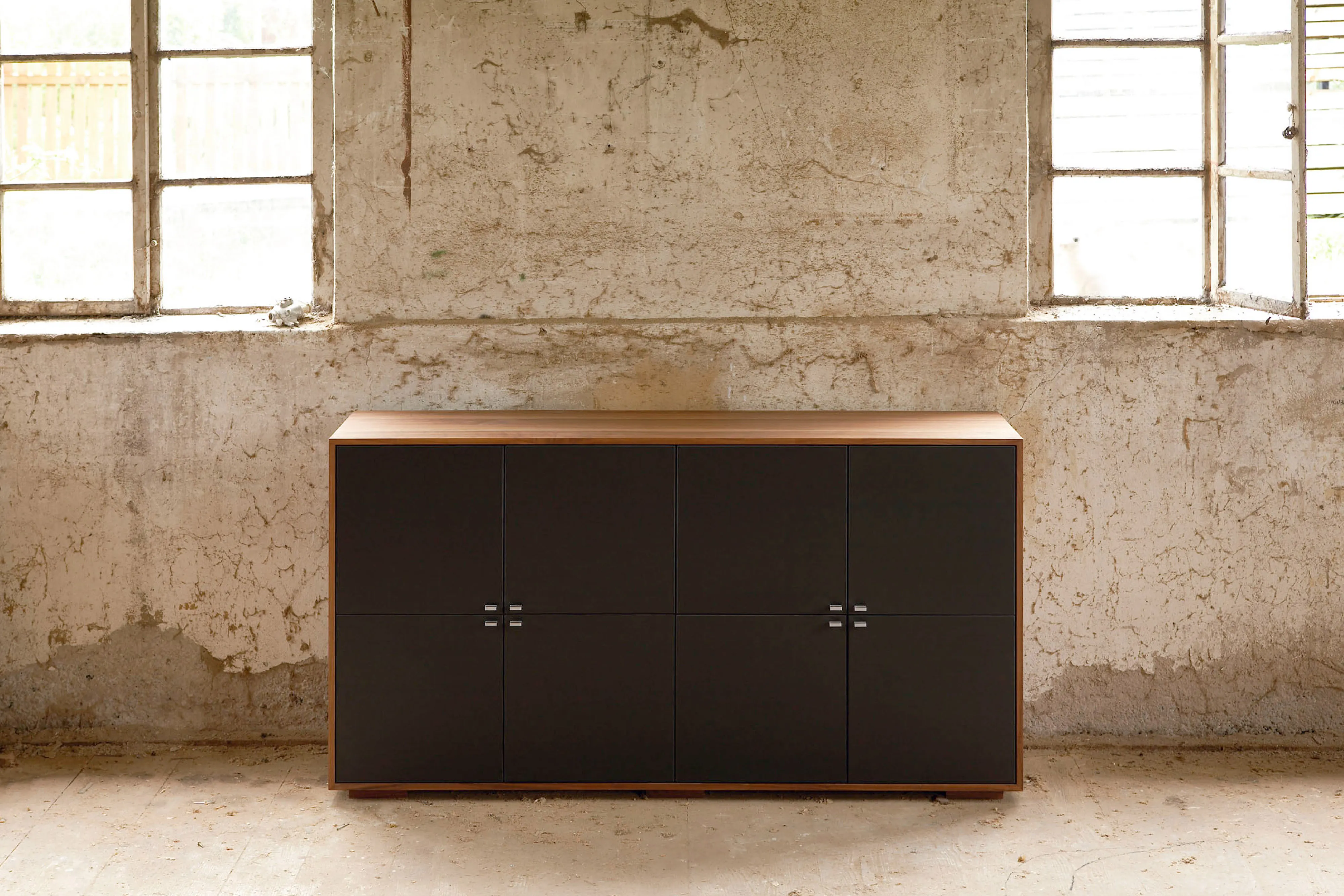 Zweifarbiges Sideboard mit dunklen Fronten und Holzkorpus vor einer rustikalen, unverputzten Wand.