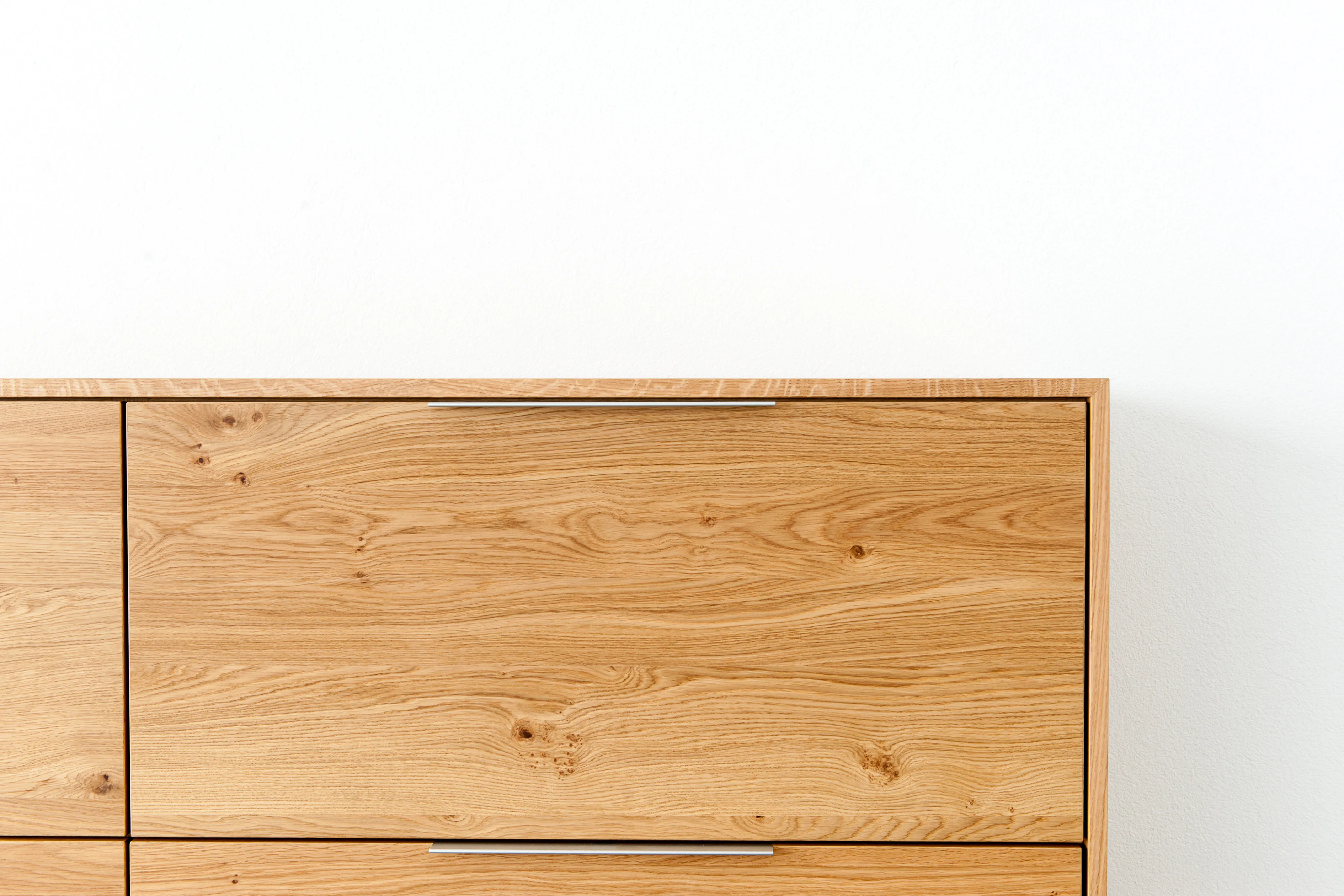 Nahaufnahme der Oberkante eines Eichenholz-Sideboards mit dezenter Metall-Griffleiste und natürlicher Holzmaserung.