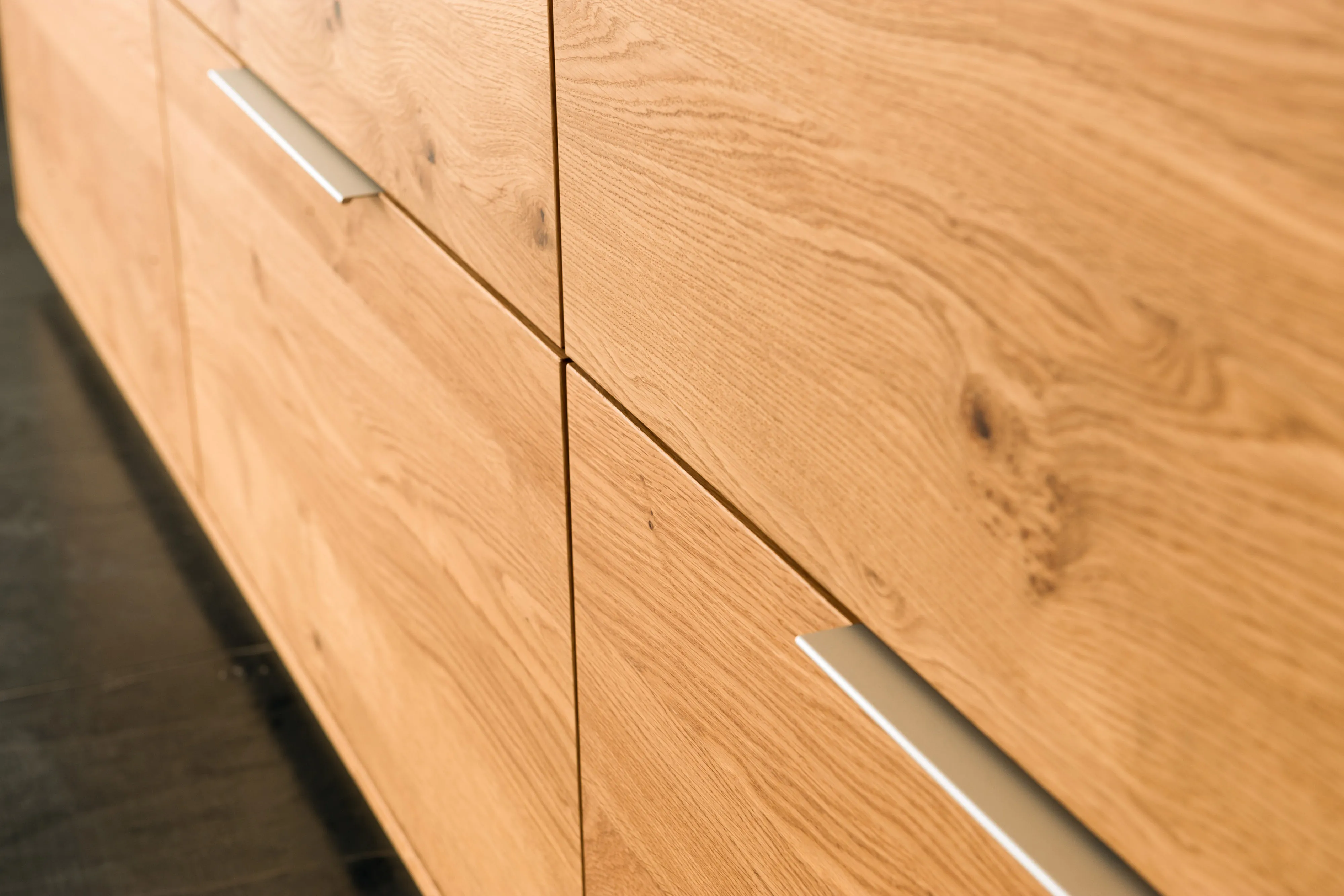 Detailansicht der Schrankfront eines Holz-Sideboards aus Eiche mit flachen, alufarbenen Griffleisten.