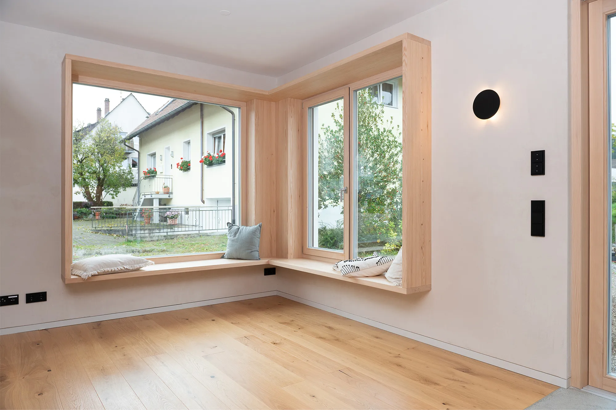 Großes Eck-Sitzfenster mit Holzverkleidung, gemütlichen Kissen und Blick auf eine ruhige Wohnstraße.
