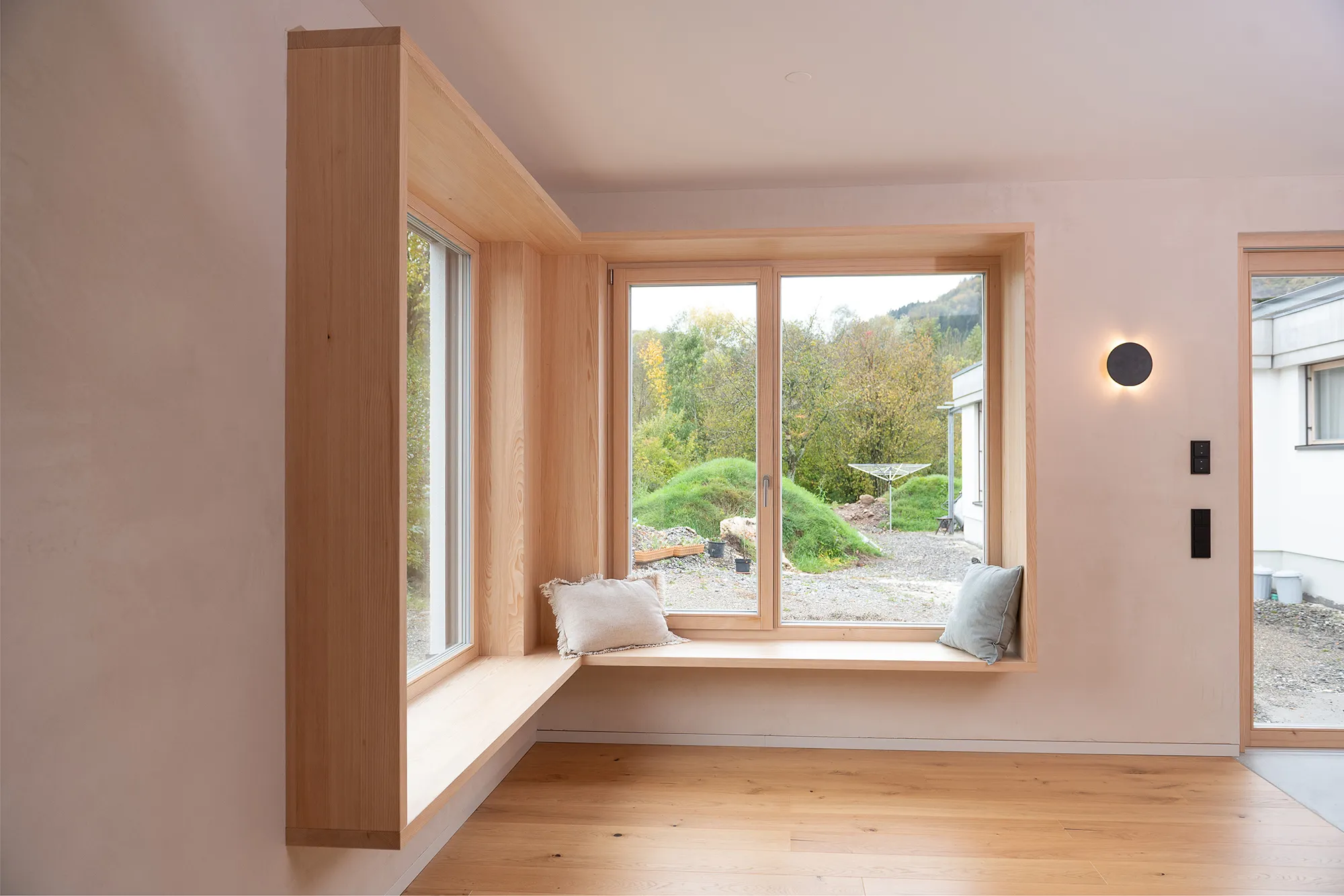 Seitenansicht eines maßgefertigten Eck-Sitzfensters aus hellem Holz mit gemütlichen Kissen.