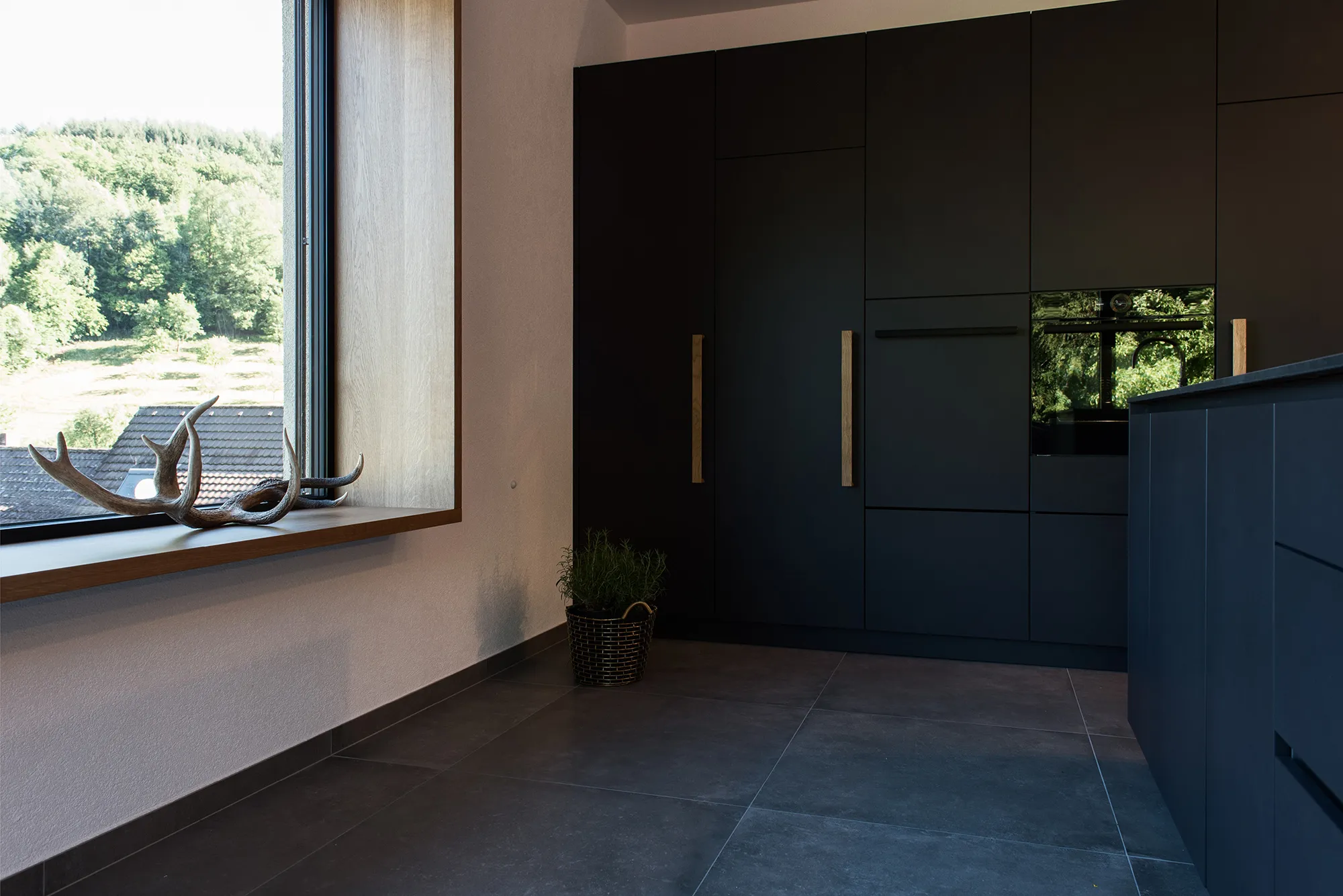 Sitzfenster mit Eichenholz-Laibung und Hirschgeweih als Deko in einer modernen, schwarzen Küche.
