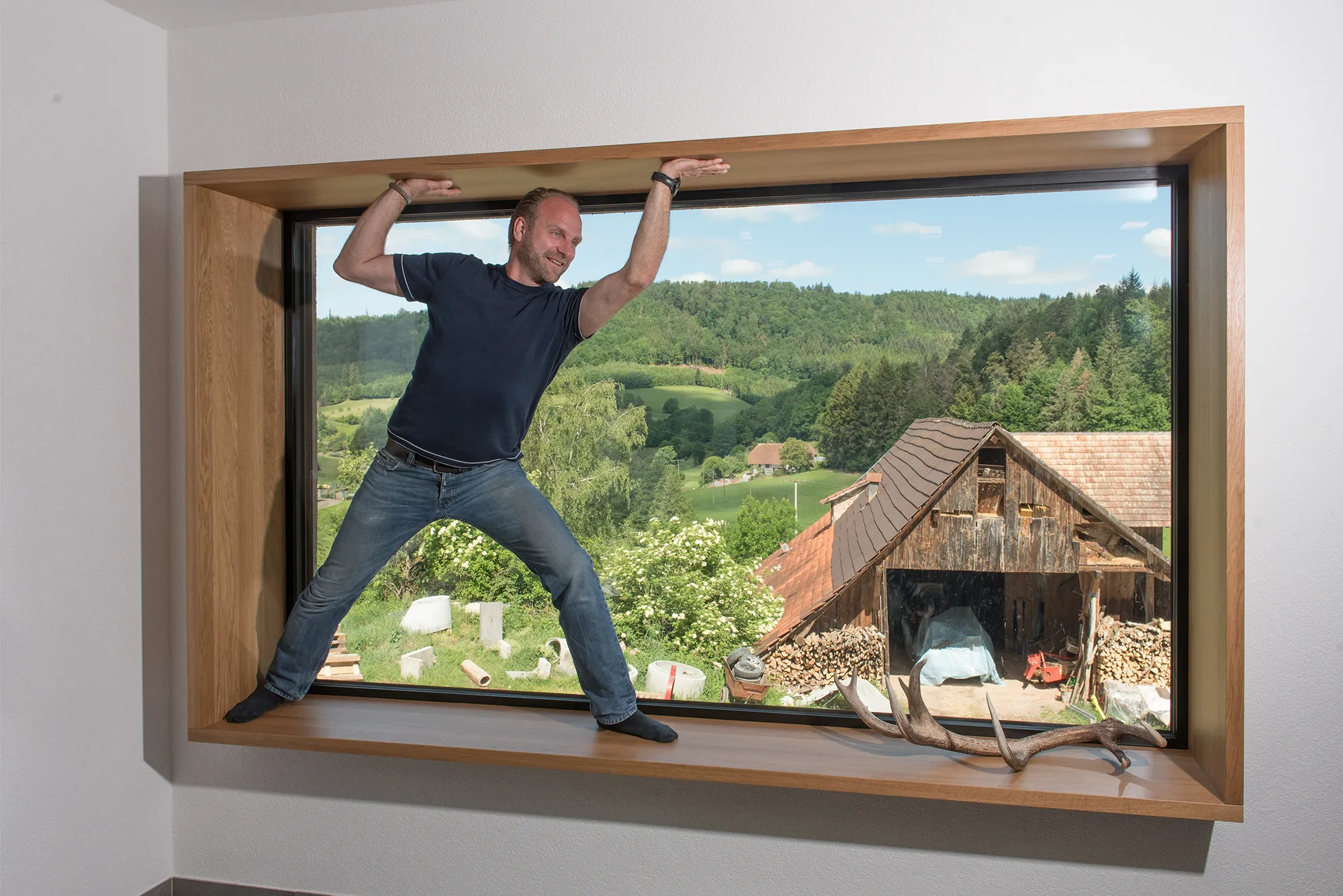 Bernhard Frankenhauser steht im tiefen Holzrahmen eines großen Panorama-Sitzfensters mit malerischem Blick auf die Natur.