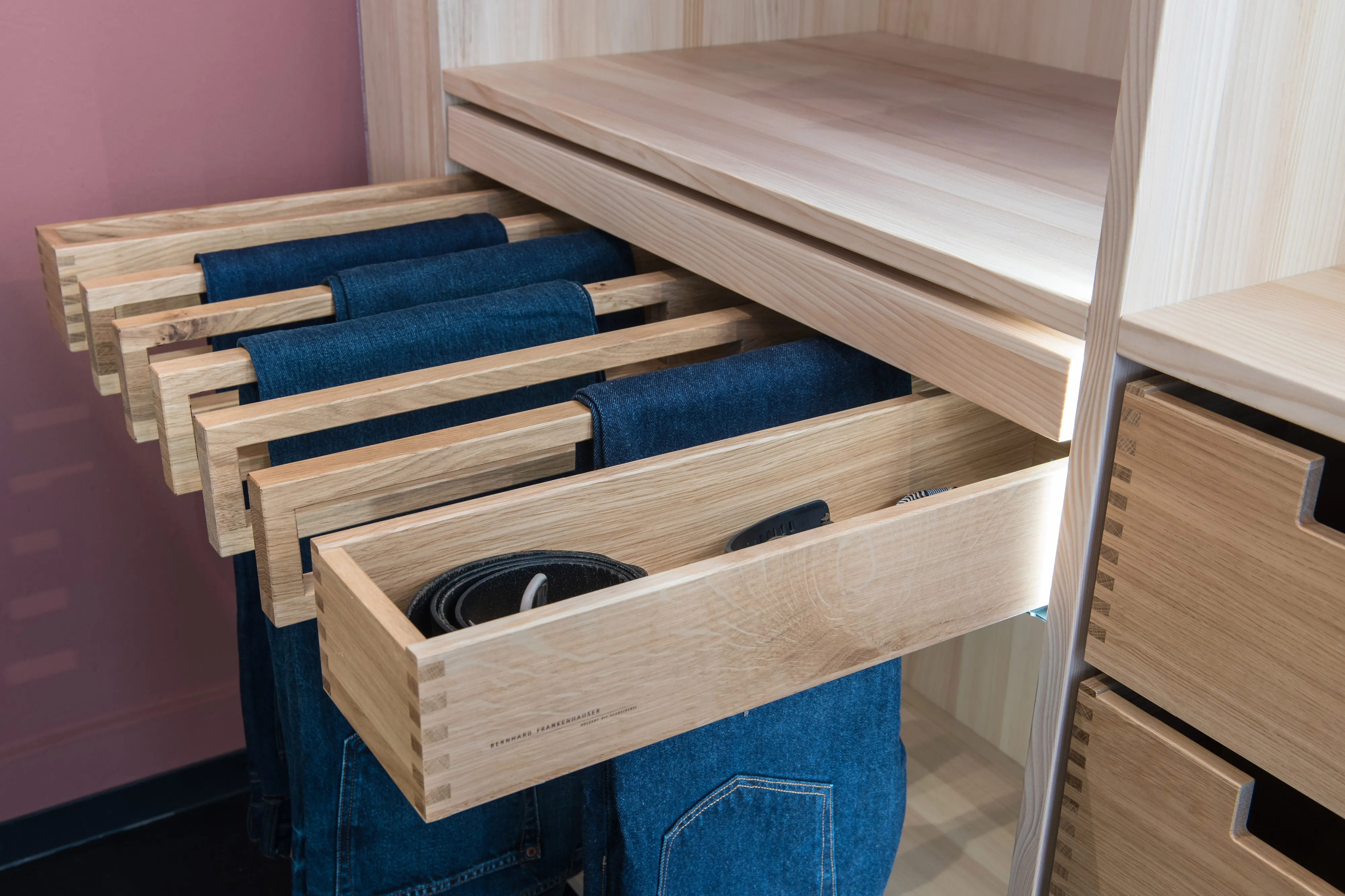 Nahaufnahme des ausziehbaren Hosenhalters aus Holz mit aufgehängten Jeans und Zubehörschublade im Kleiderschrank.