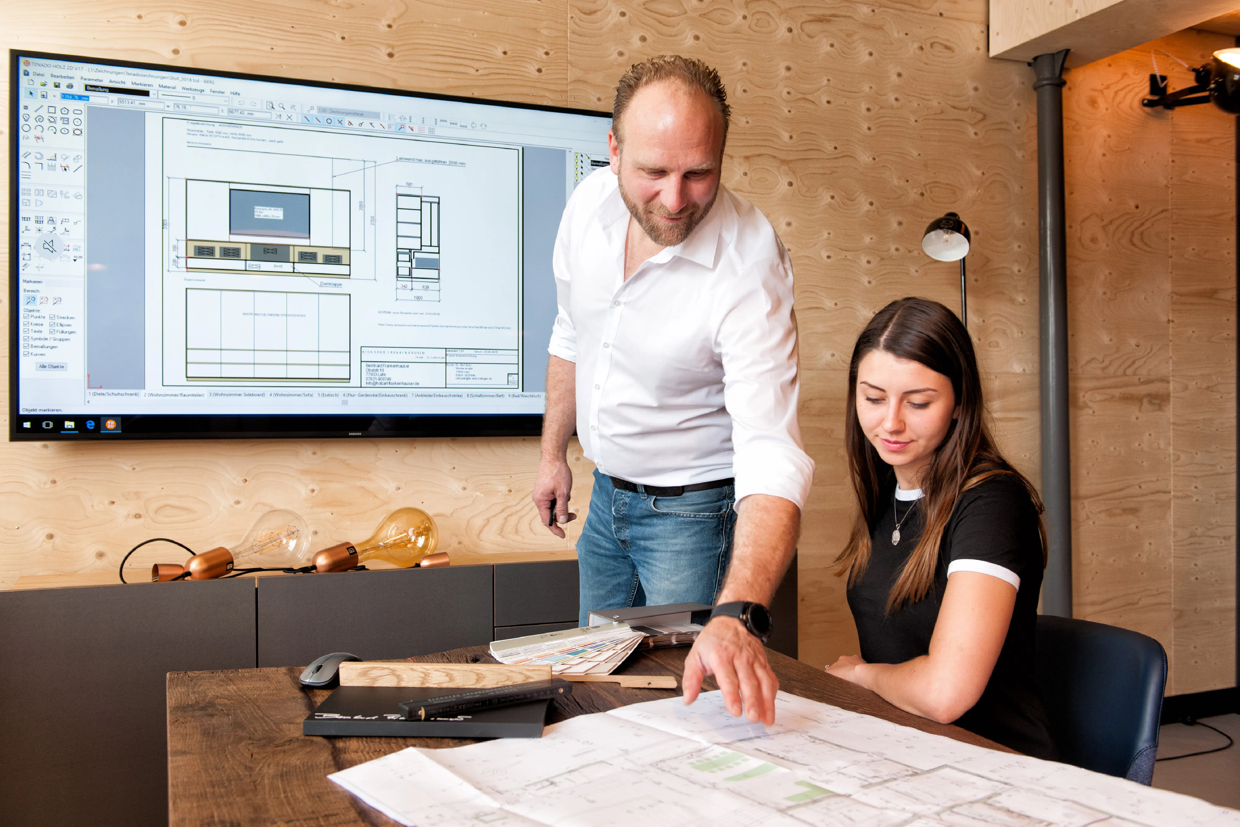 Persönliche Kundenberatung am Besprechungstisch mit Grundrissplan und digitaler 3D-Möbelplanung auf großem Bildschirm.