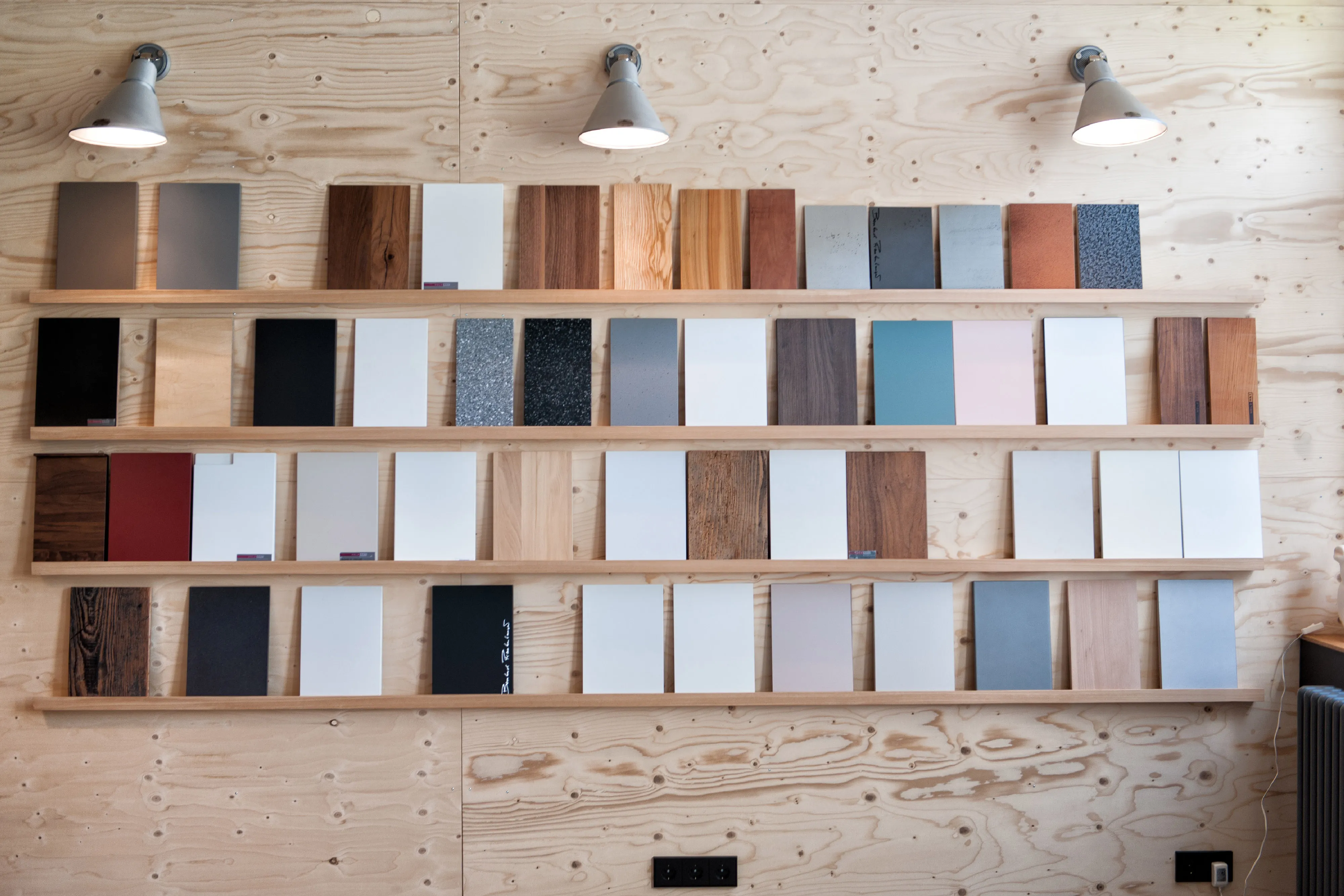 Materialwand im Schauraum mit einer großen Auswahl an Holz-, Farb- und Oberflächenmustern auf Holzregalen.