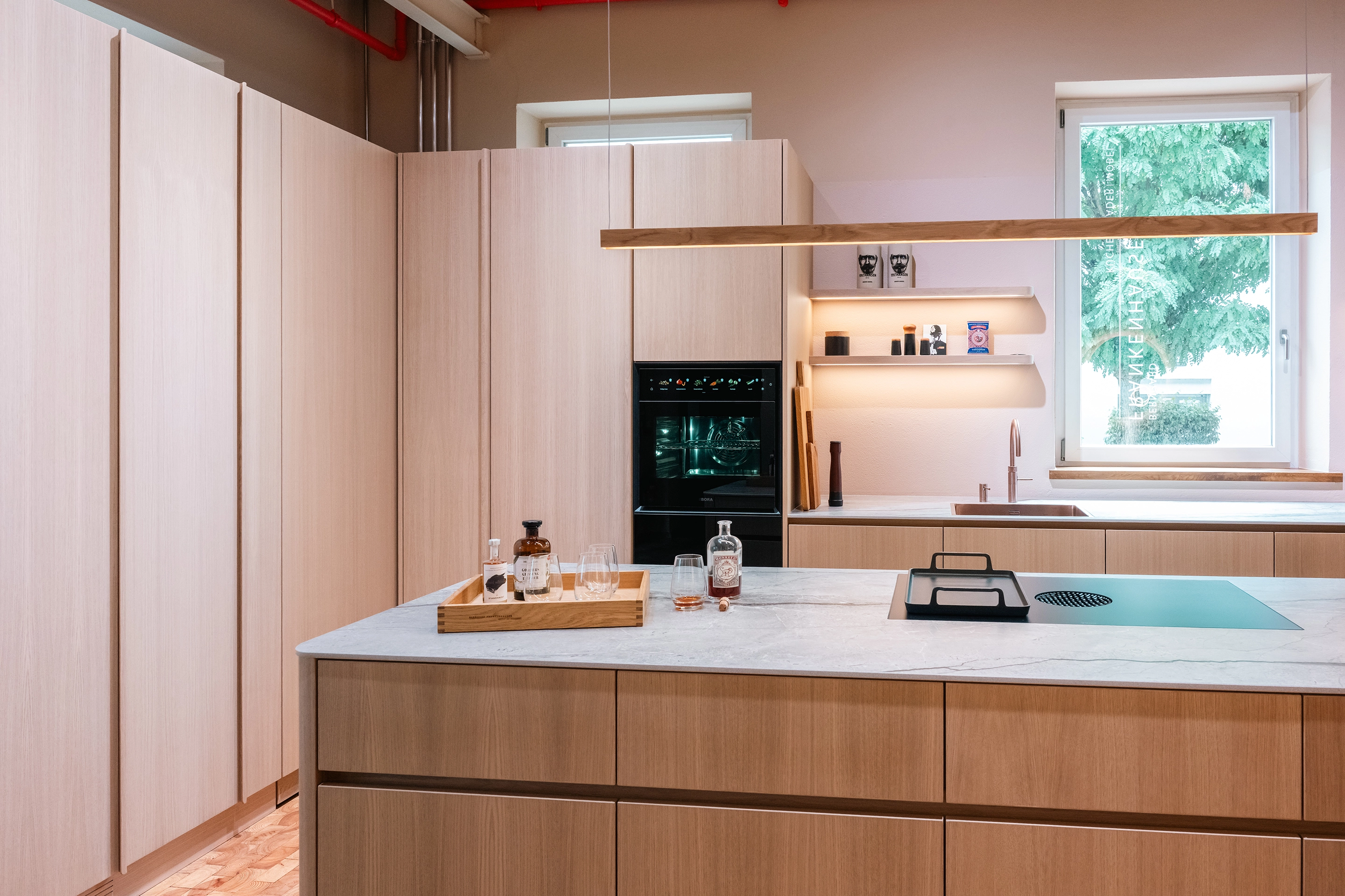 Frontalansicht einer Holzküche mit BORA Einbaubackofen, Quooker Armatur und Hera LED-Wandregalen.