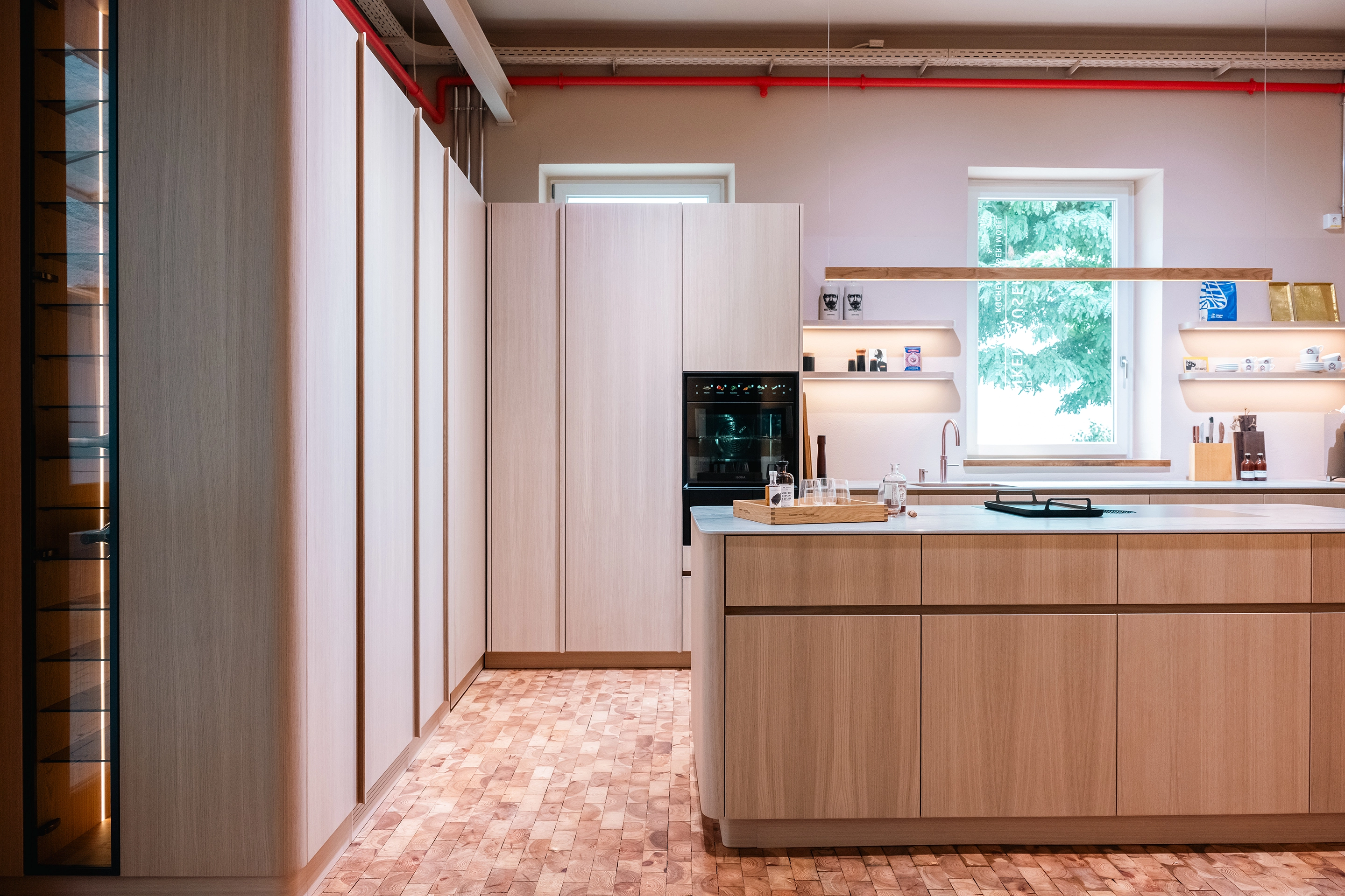 Frontale Gesamtansicht der Showroom-Küche mit BORA Kochfeld, Quooker Armatur und stimmungsvoller Olev Beleuchtung.
