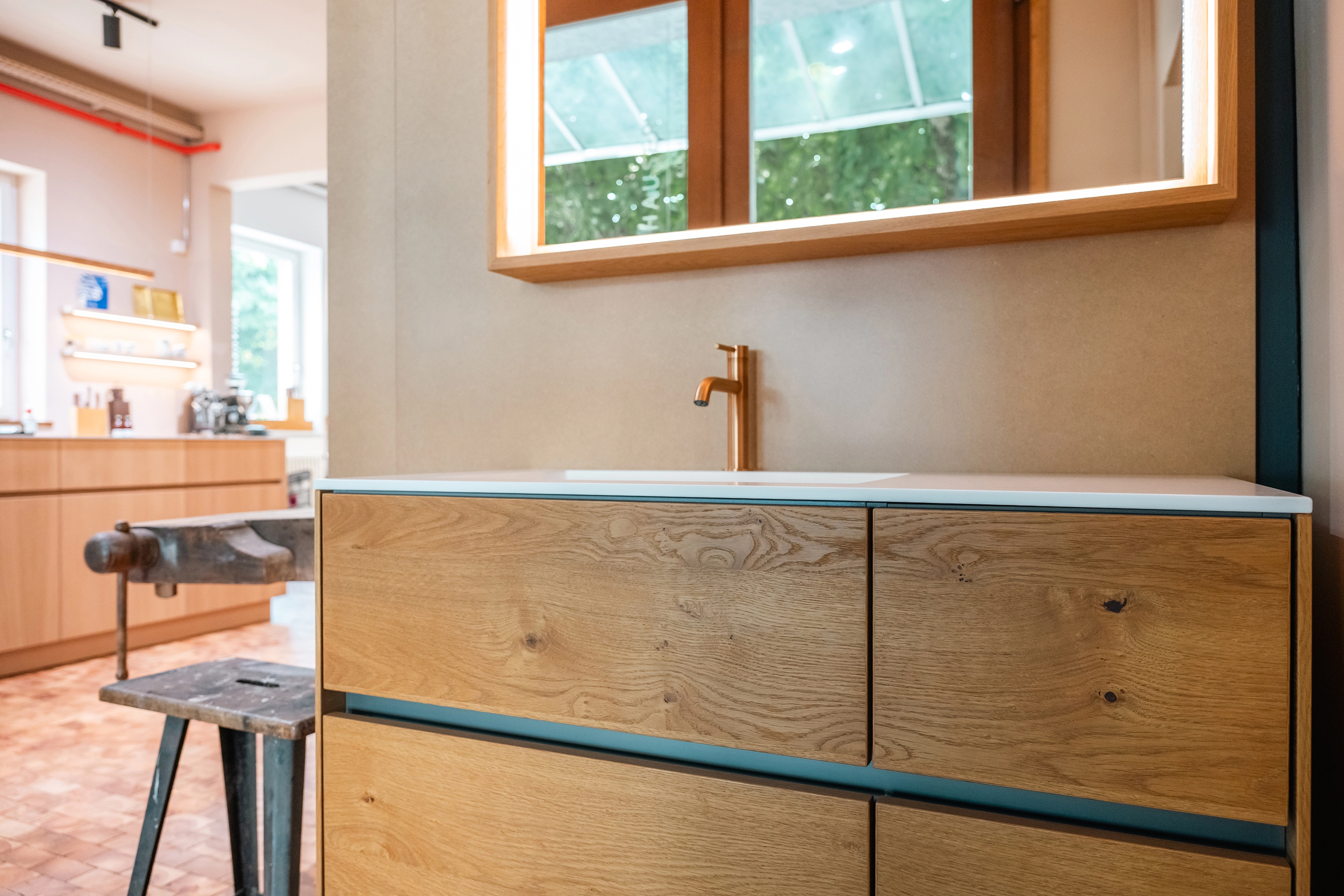 Moderner Holz-Waschtisch mit MGS Armatur, beleuchtetem Olev Spiegel und rustikaler Werkbank im Hintergrund.