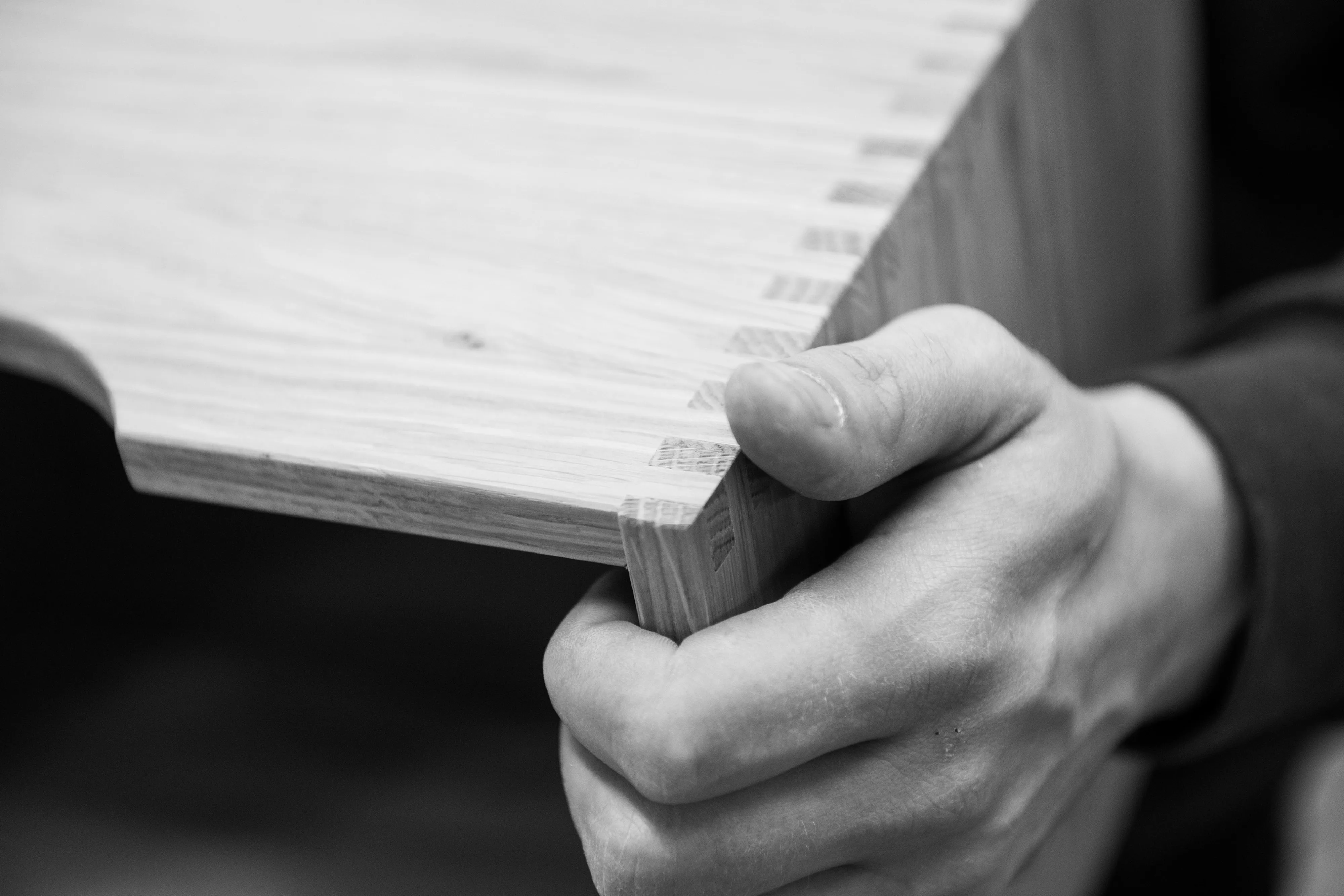Detailaufnahme in Schwarz-Weiß: Eine Hand prüft die präzise gezinkte Eckverbindung eines Holzschubs.
