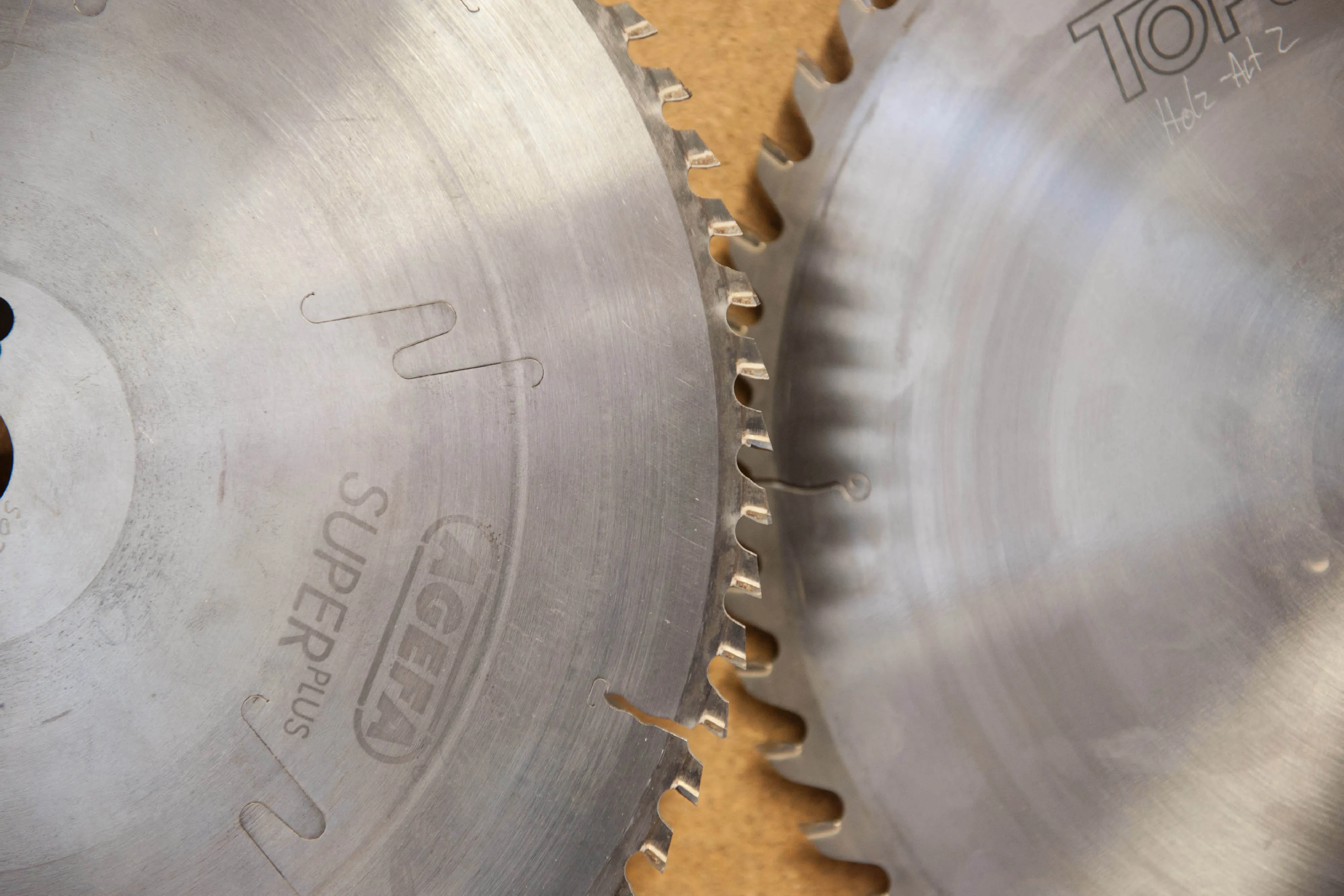 Nahaufnahme von zwei ineinandergreifenden, scharfen Profi-Kreissägeblättern aus Metall auf einer Werkbank.