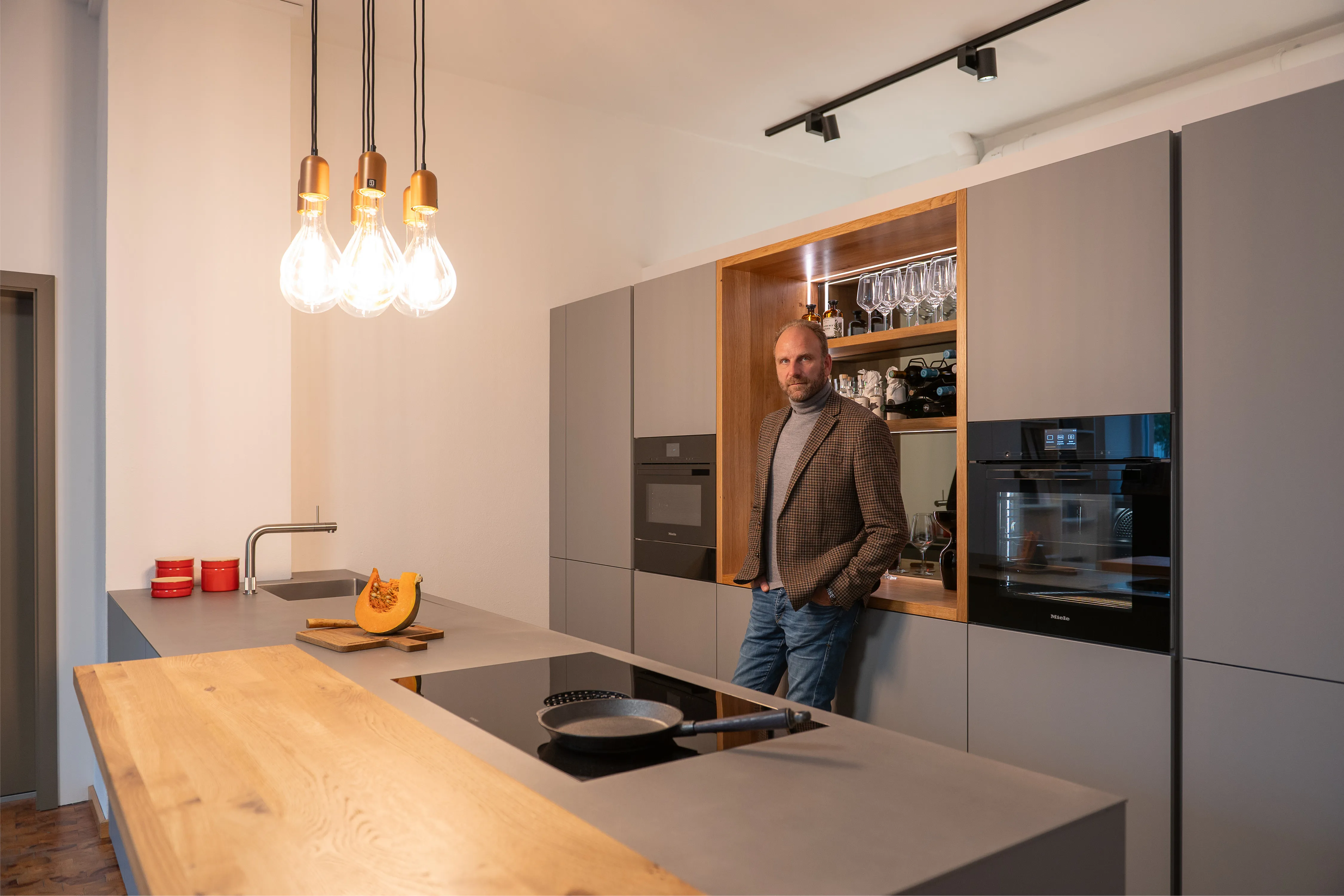 Bernhard Frankenhauser lehnt an einer grauen Kücheninsel mit Eichenholz-Aufsatz in einer modernen Showroom-Küche